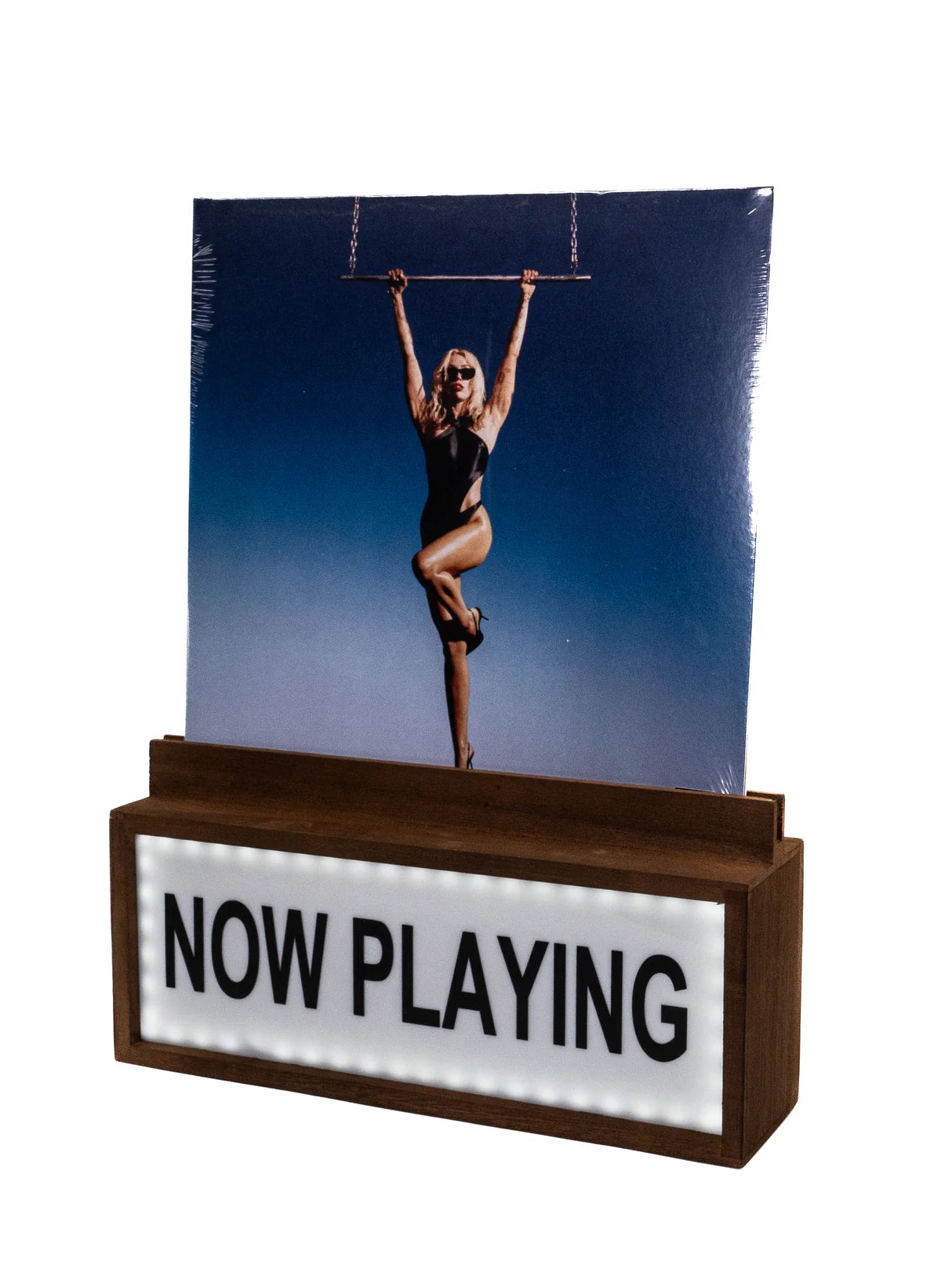 Eine Schallplatte in einer Holzhalterung mit beleuchtetem Schild "NOW PLAYING", darauf eine Frau an einer Stange.