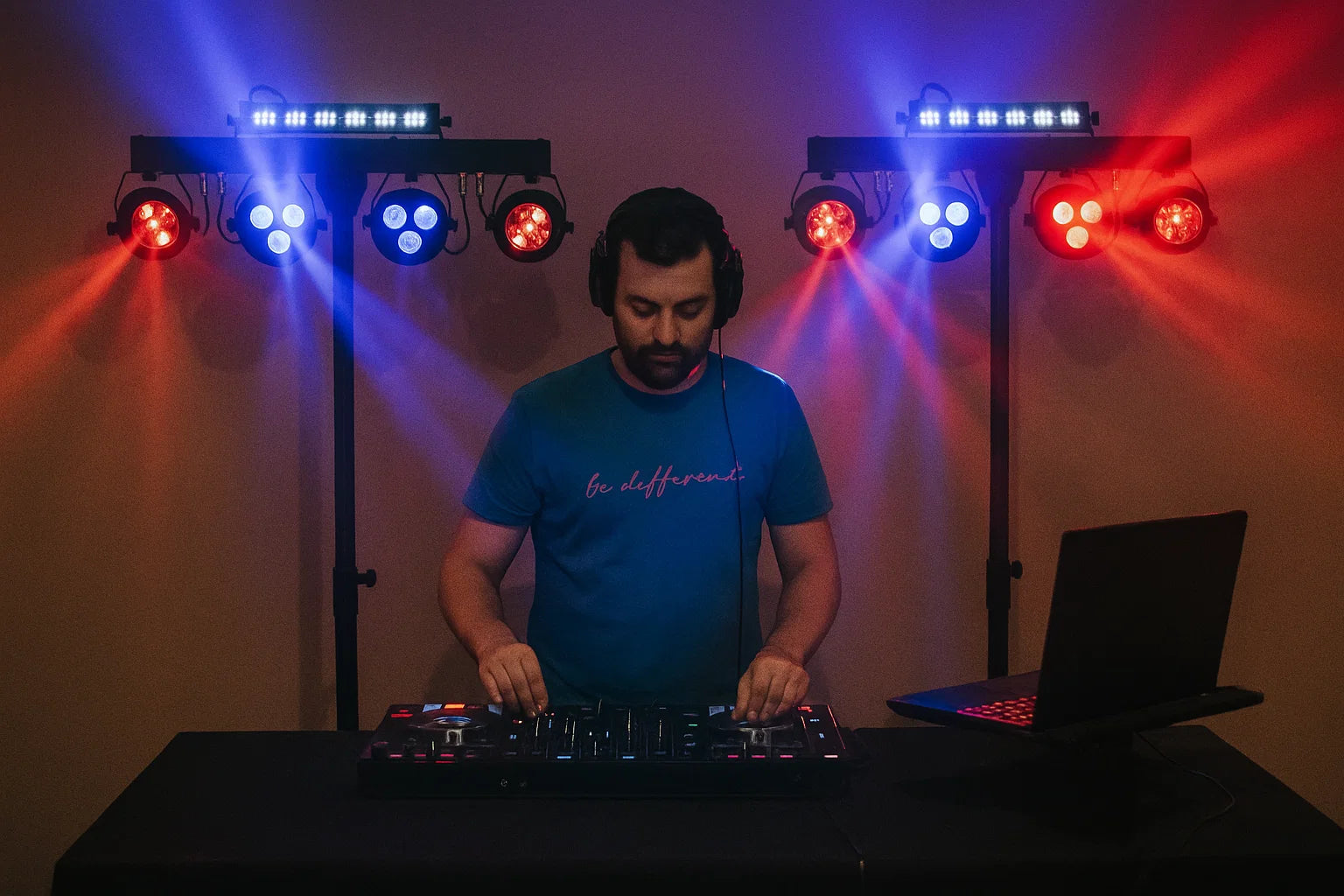 Ein DJ mit Kopfhörern legt Musik an einem Mischpult auf, umrahmt von bunten Bühnenlichtern.