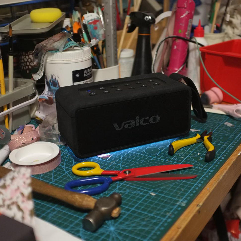 Ein schwarzer Valco Bluetooth-Lautsprecher auf einer unordentlichen Werkbank mit Schere, Zange, Hammer und Kunstbedarf.