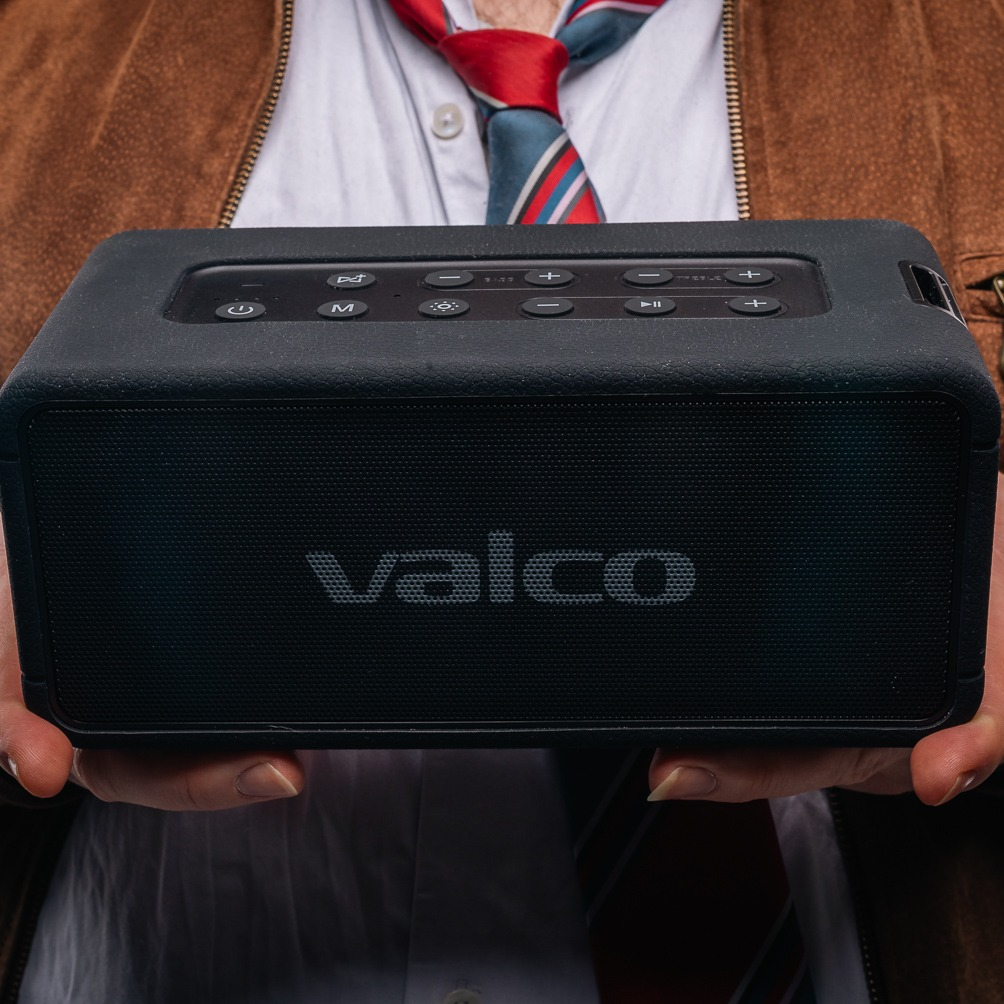 Eine Person hält einen schwarzen kabellosen Valco-Lautsprecher mit oberen Steuertasten vor sich.