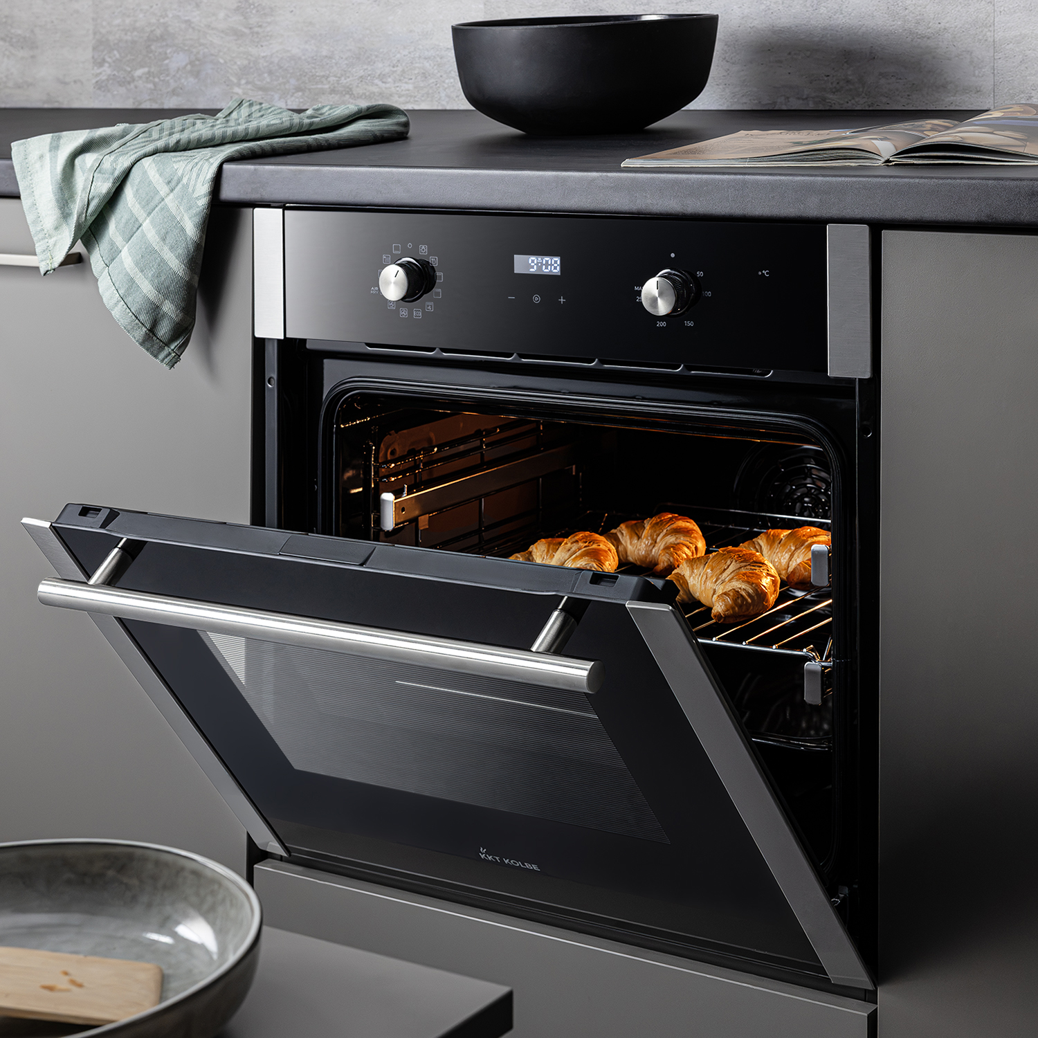 Offener Backofen mit Croissants auf dem Rost, auf der Arbeitsplatte liegen eine Schüssel und ein Handtuch.