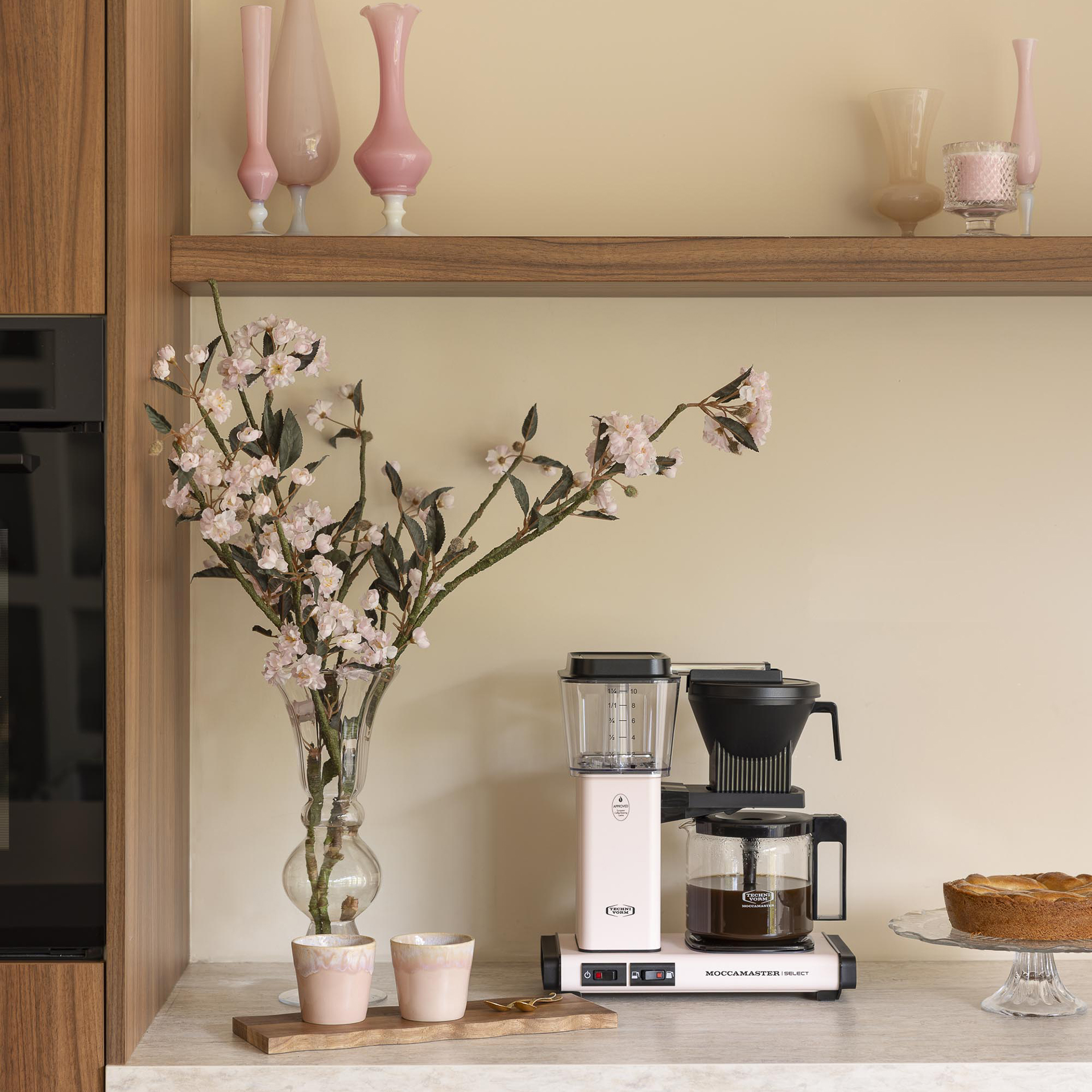 Macchina da caffè rosa con fiori in vaso e tazze su un piano cucina.