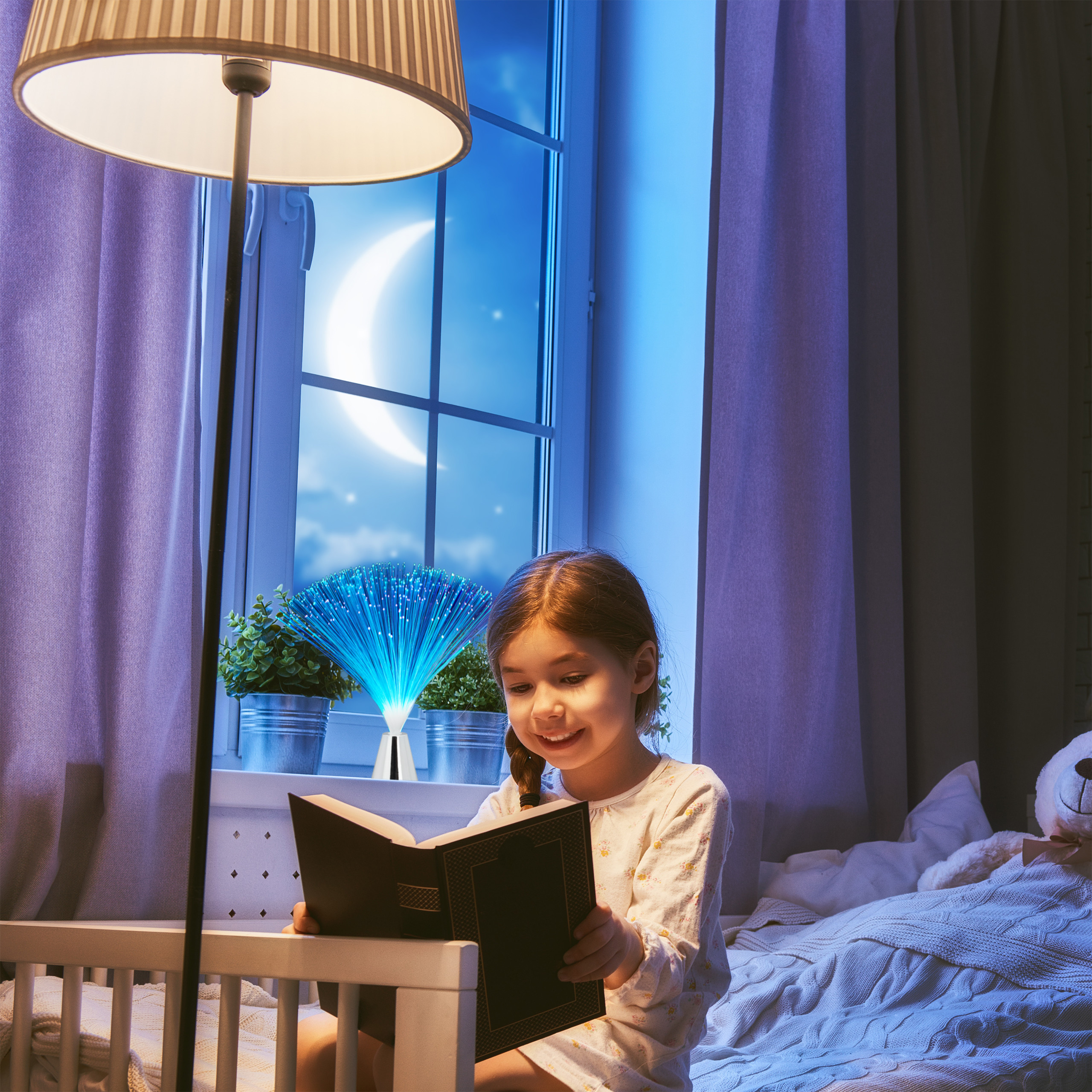 Ein junges Mädchen liest nachts im Bett bei Lampenlicht ein Buch, während draußen der Mond am Fenster scheint.