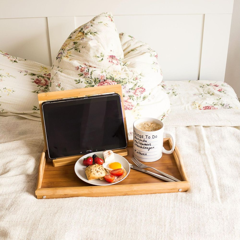 Ein hölzernes Tablett im Bett mit Tablet, Frühstück und Kaffeetasse.
