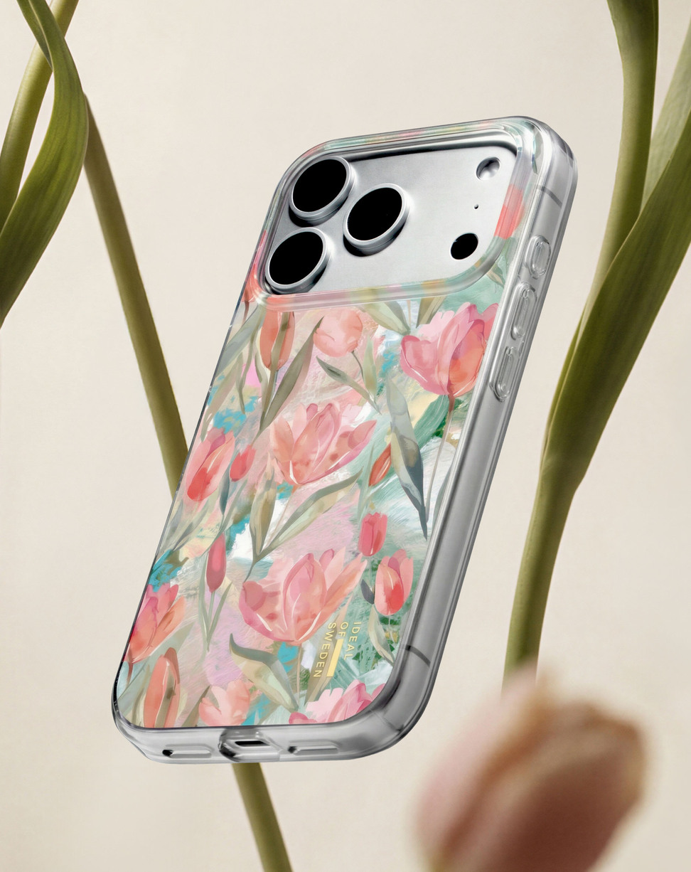 Smartphone in einer rosa Blumenhülle, vertikal zwischen grünen Tulpenstielen vor hellem Hintergrund.