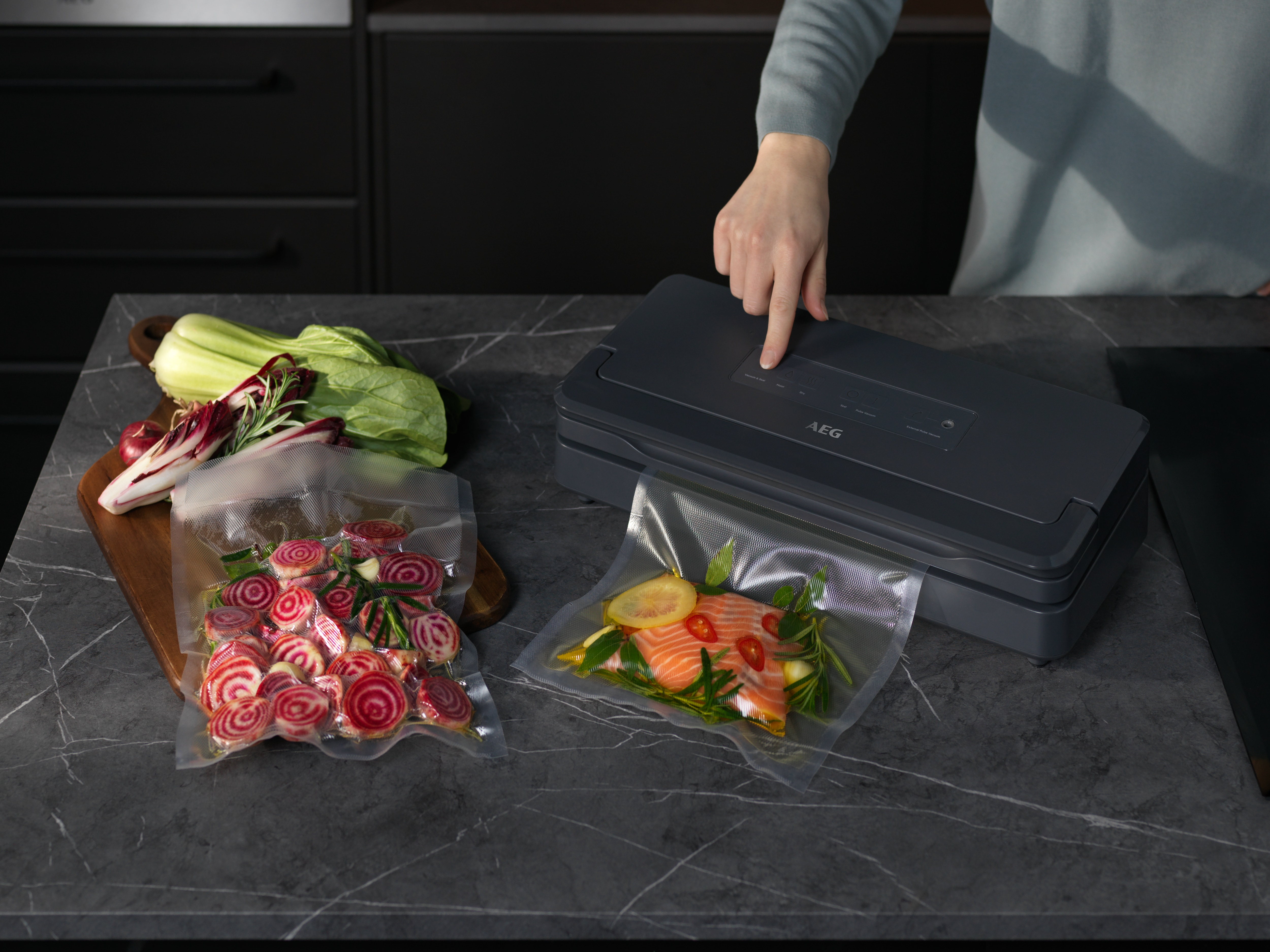 Una persona opera una envasadora al vacío en una encimera de cocina con alimentos sellados.