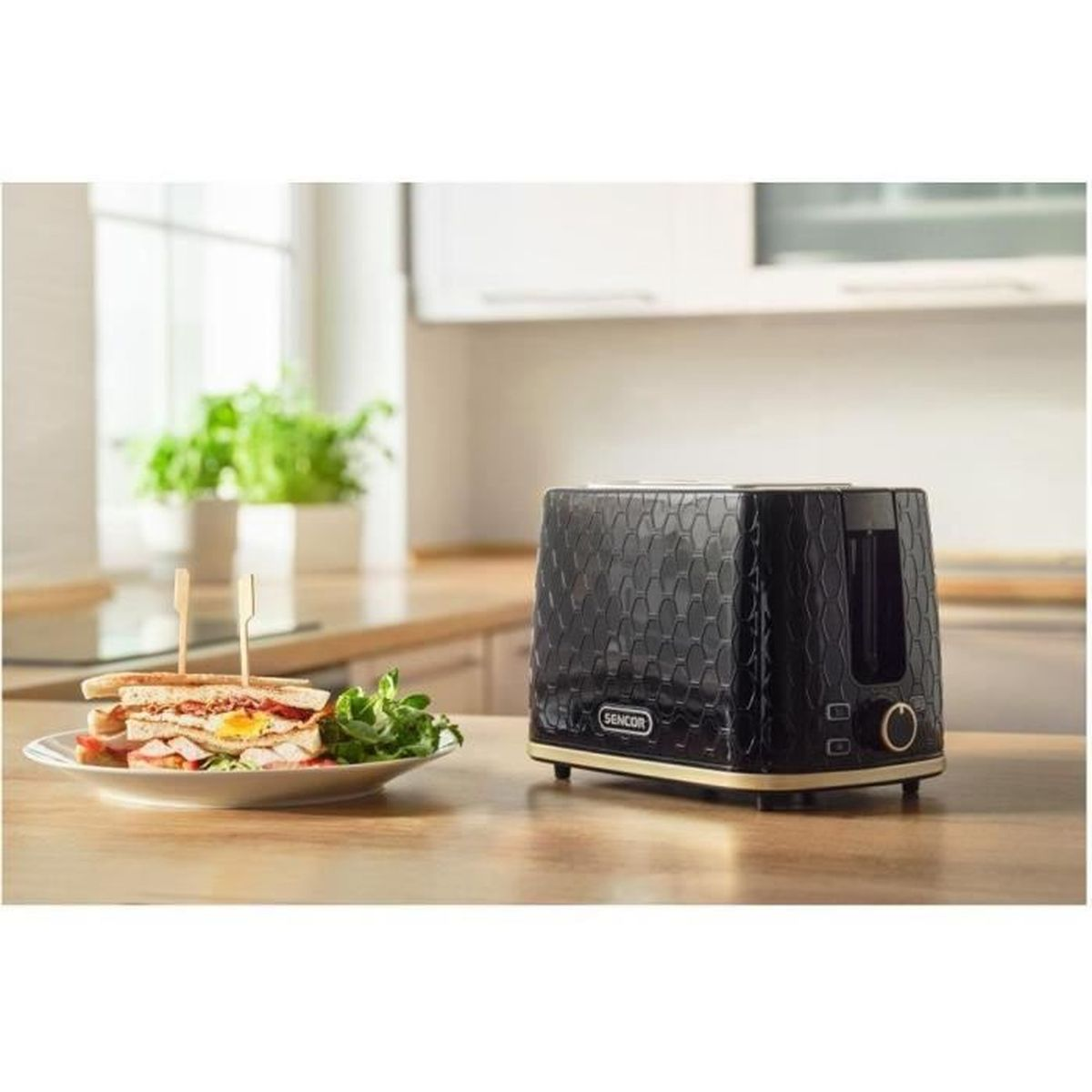 Un tostapane nero e un piatto con panini sono su un piano di lavoro in legno in una cucina.