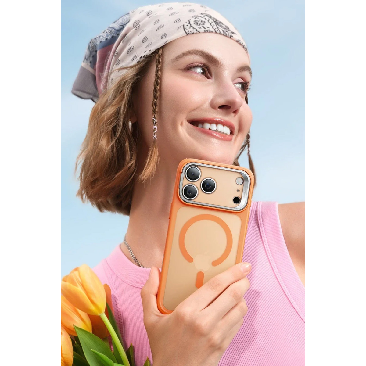 Bandana ve pembe atlet giyen kadın, turuncu telefon kılıfı ve sarı laleler tutuyor.