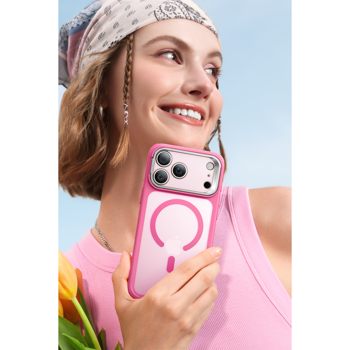 Pembe üstlü ve desenli başörtülü gülümseyen kadın, üç kameralı pembe akıllı telefon tutuyor.