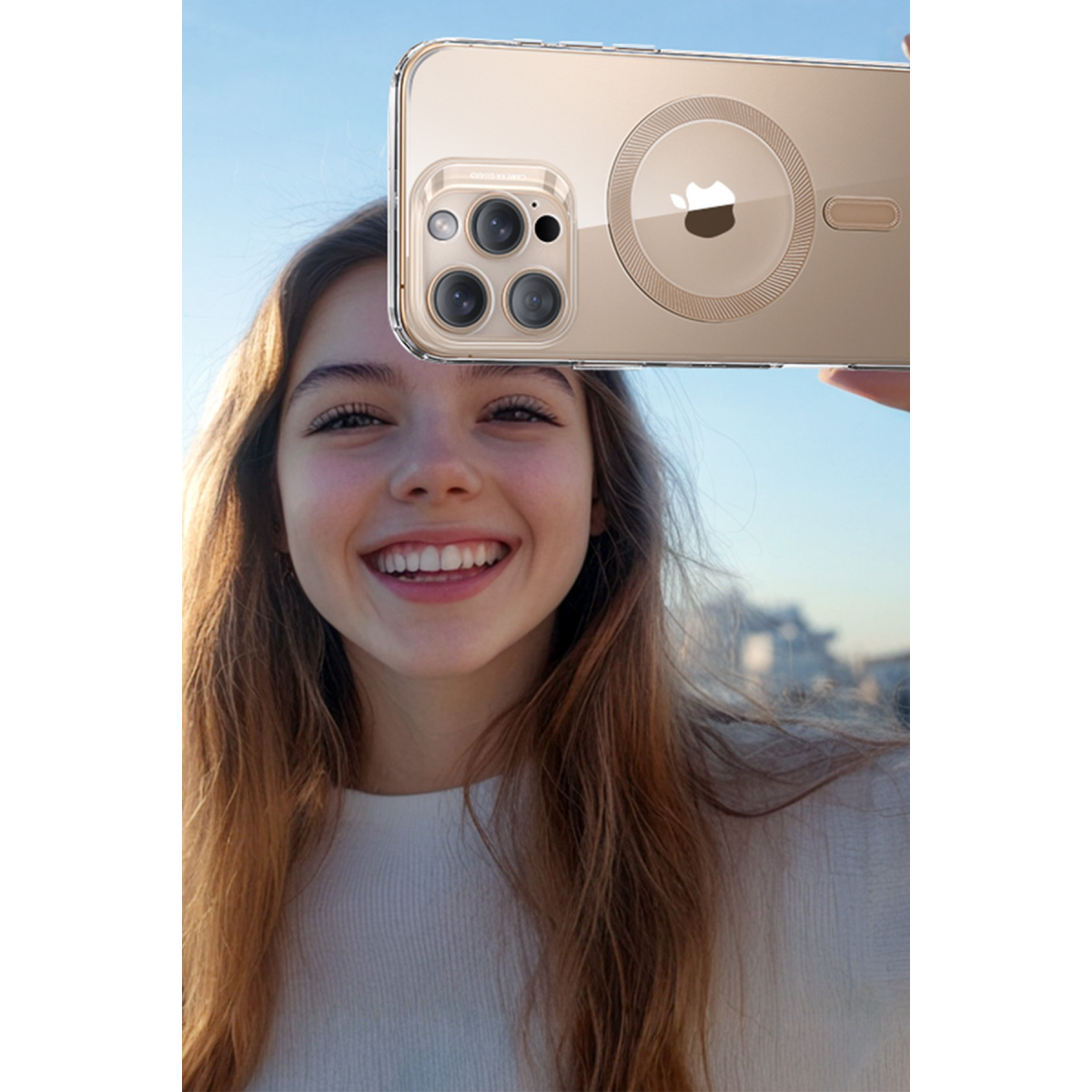 Gülüümseyen bir kadın yüzünün önünde şeffaf kılıflı altın renkli bir iPhone tutuyor.
