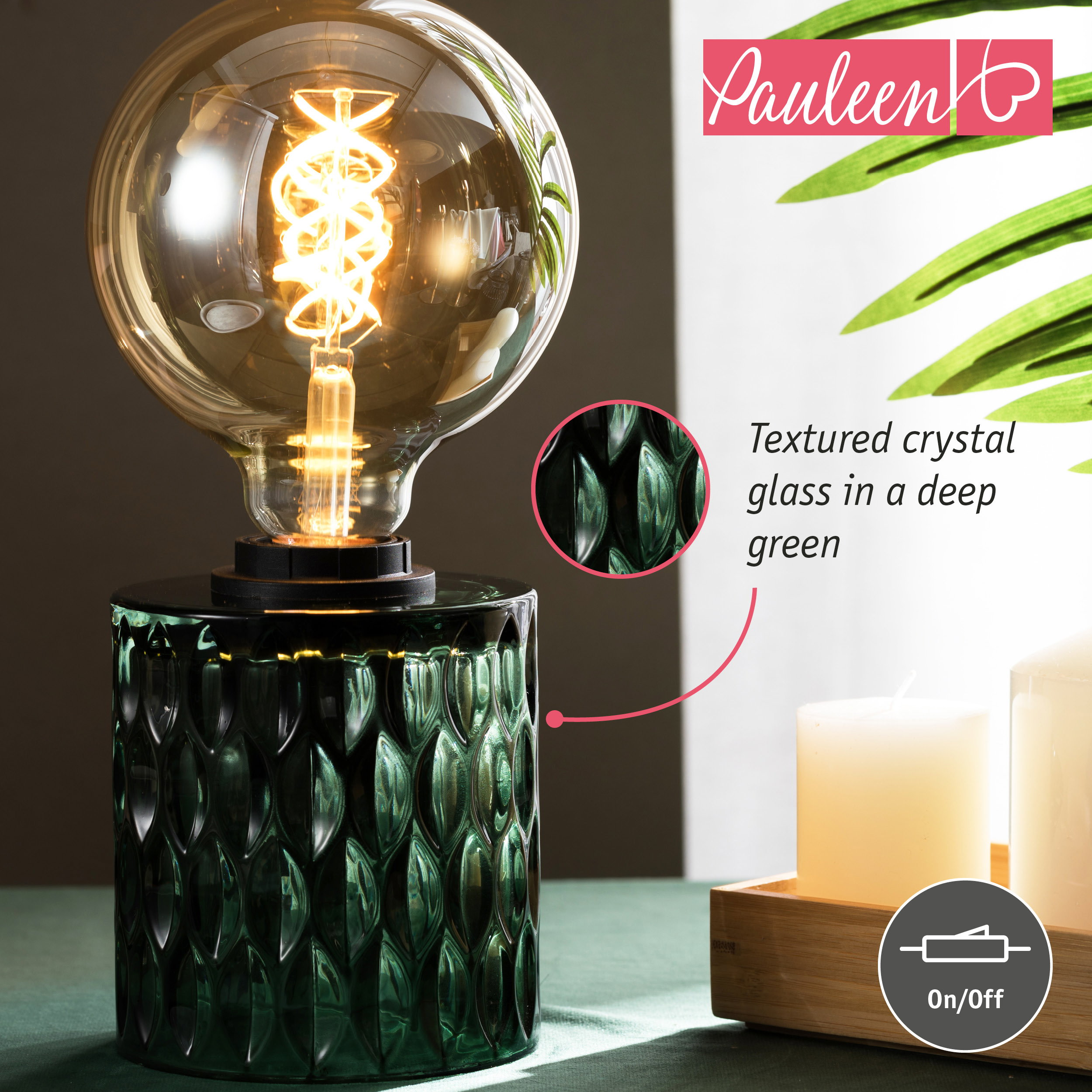 Una lampada da tavolo in vetro verde con grande lampadina, accanto a candele bianche su un vassoio.