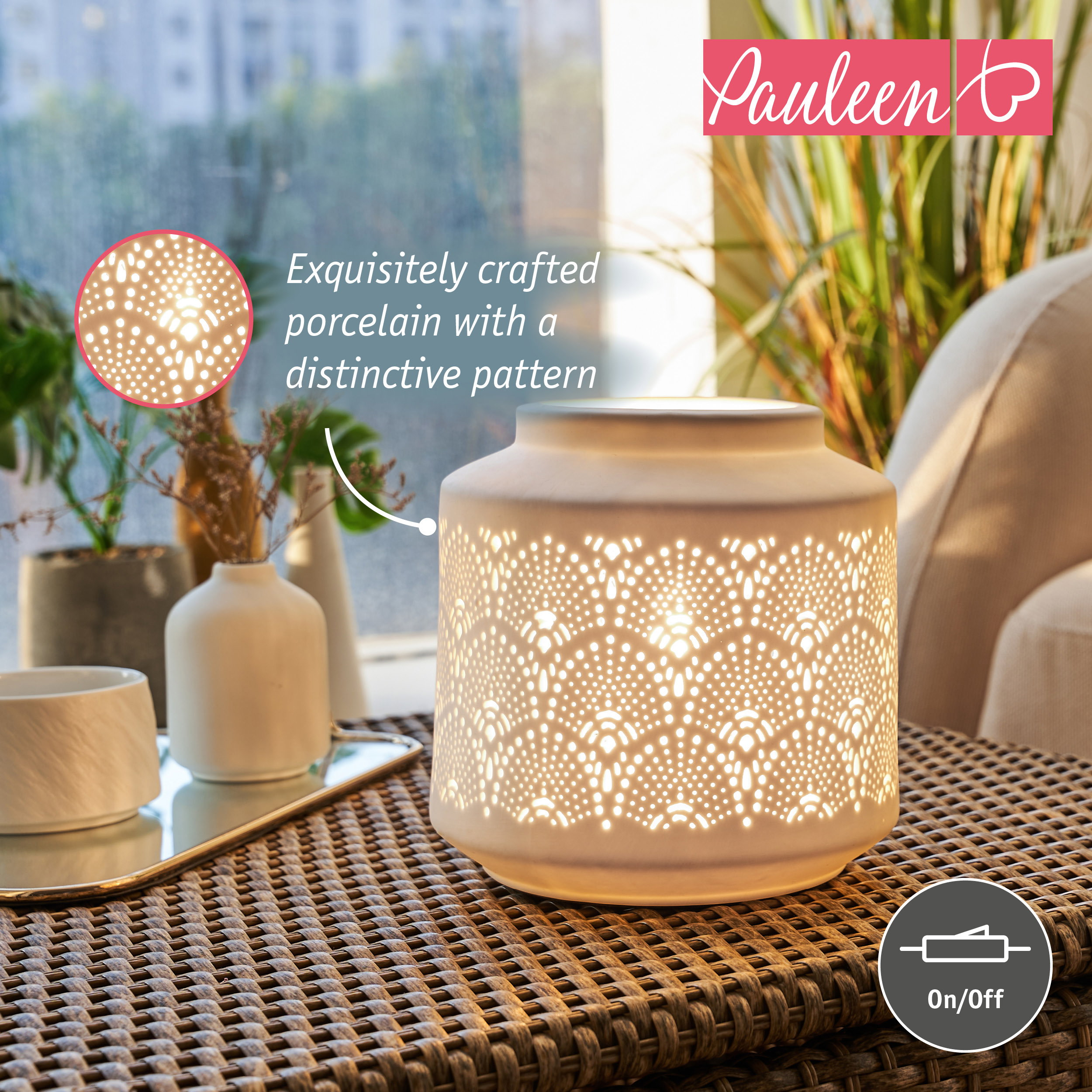Eine weiße Porzellanlampe mit feinem Muster leuchtet auf einem Rattan-Tisch, umgeben von Pflanzen und Dekoration.