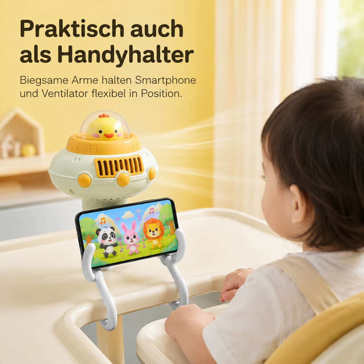 Kleinkind sitzt im Hochstuhl vor einem gelben UFO-Ventilator mit Handyhalterung, der einen Cartoon zeigt.