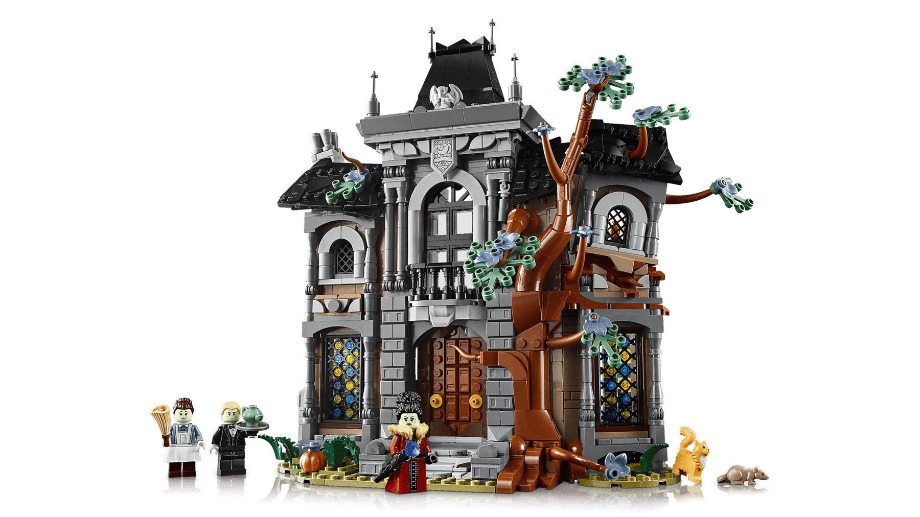 Szczegółowy nawiedzony dom Lego z szarymi cegłami, czarnymi dachami, brązowym drzewem i pięcioma minifigurkami z przodu.