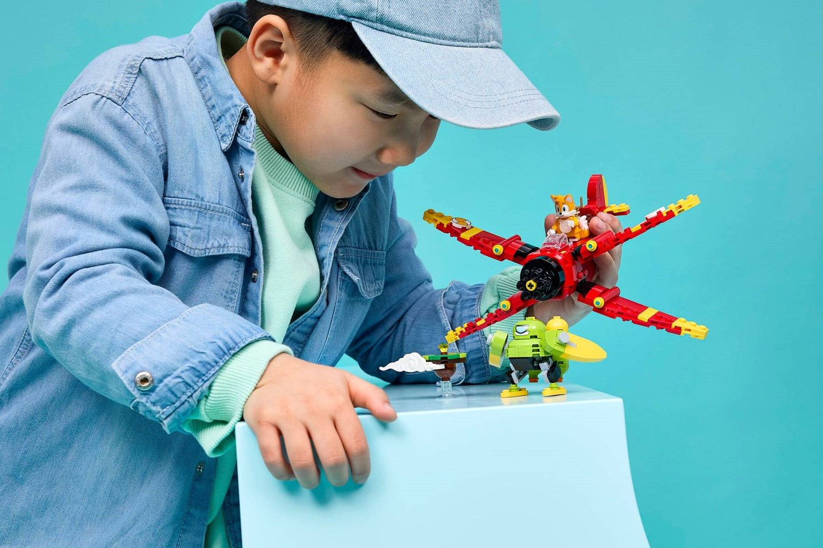 Un niño con ropa de mezclilla juega con coloridos modelos de LEGO sobre un fondo azul.