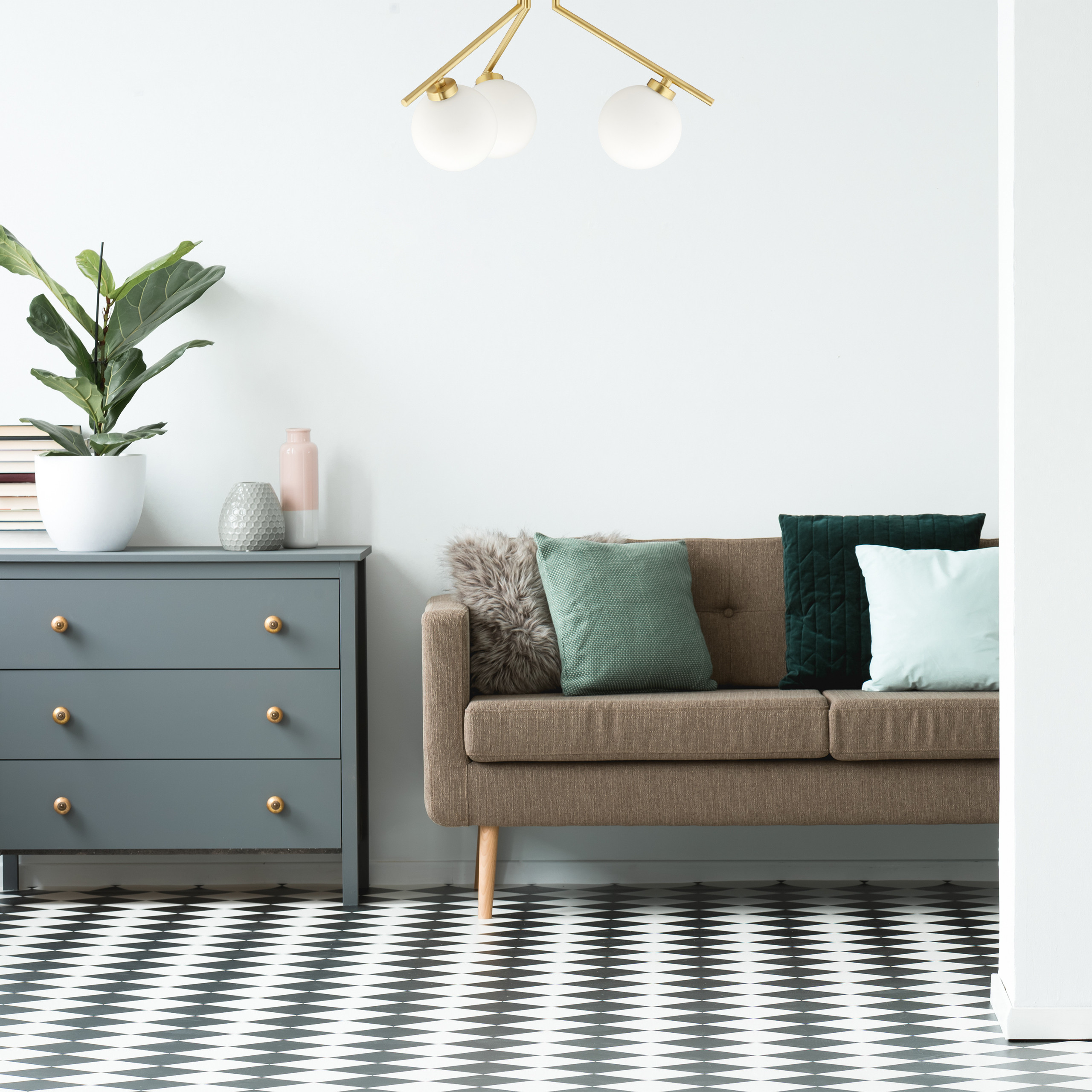 Ein braunes Sofa mit Kissen steht neben einer grauen Kommode vor einer weißen Wand und einem schwarz-weißem Fliesenboden.