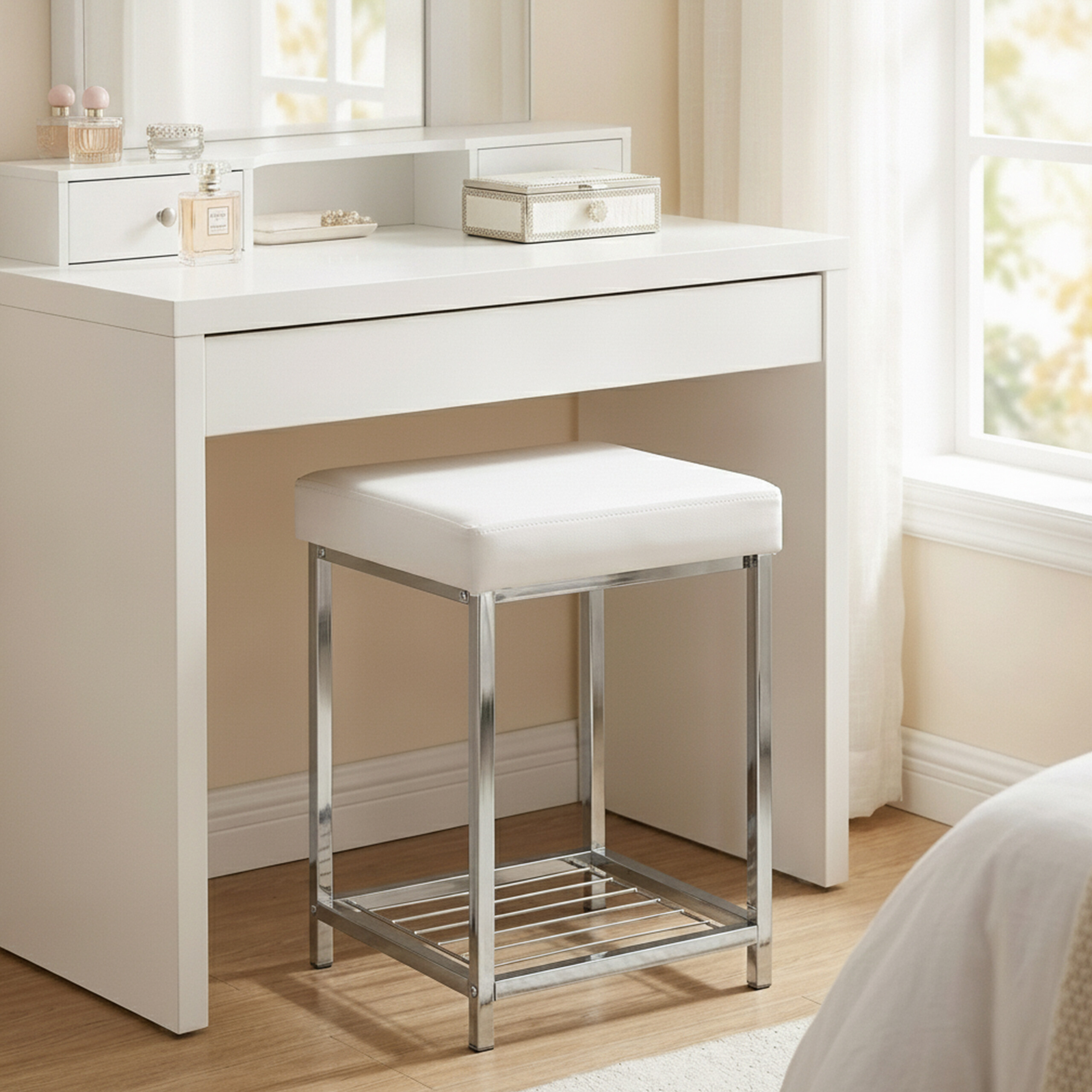 Ein weißer Schminktisch mit Spiegel und ein passender Hocker mit verchromten Beinen stehen in einem hellen Zimmer.