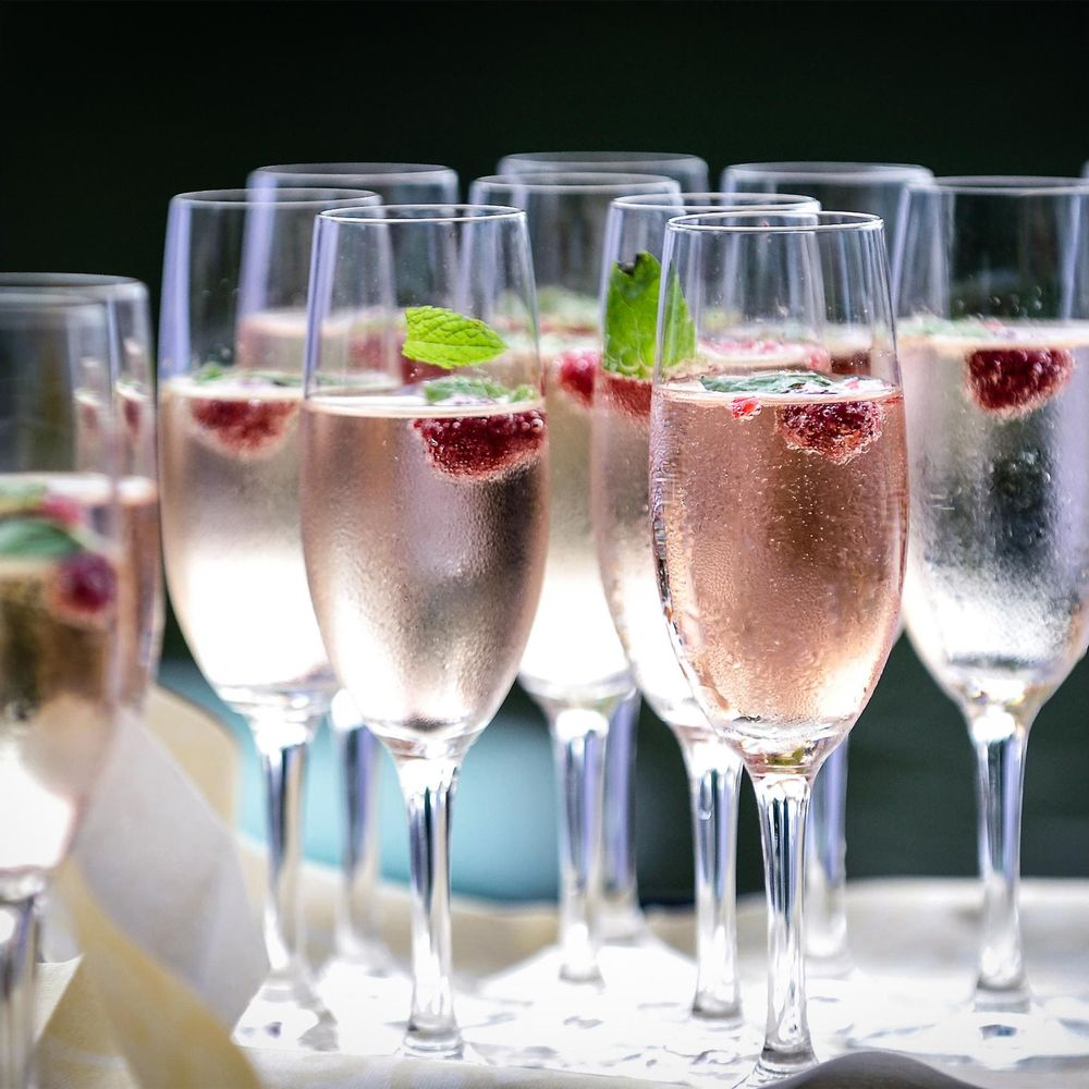 Mehrere Sektgläser gefüllt mit roséfarbenem Schaumwein, Himbeeren und Minzblättern.