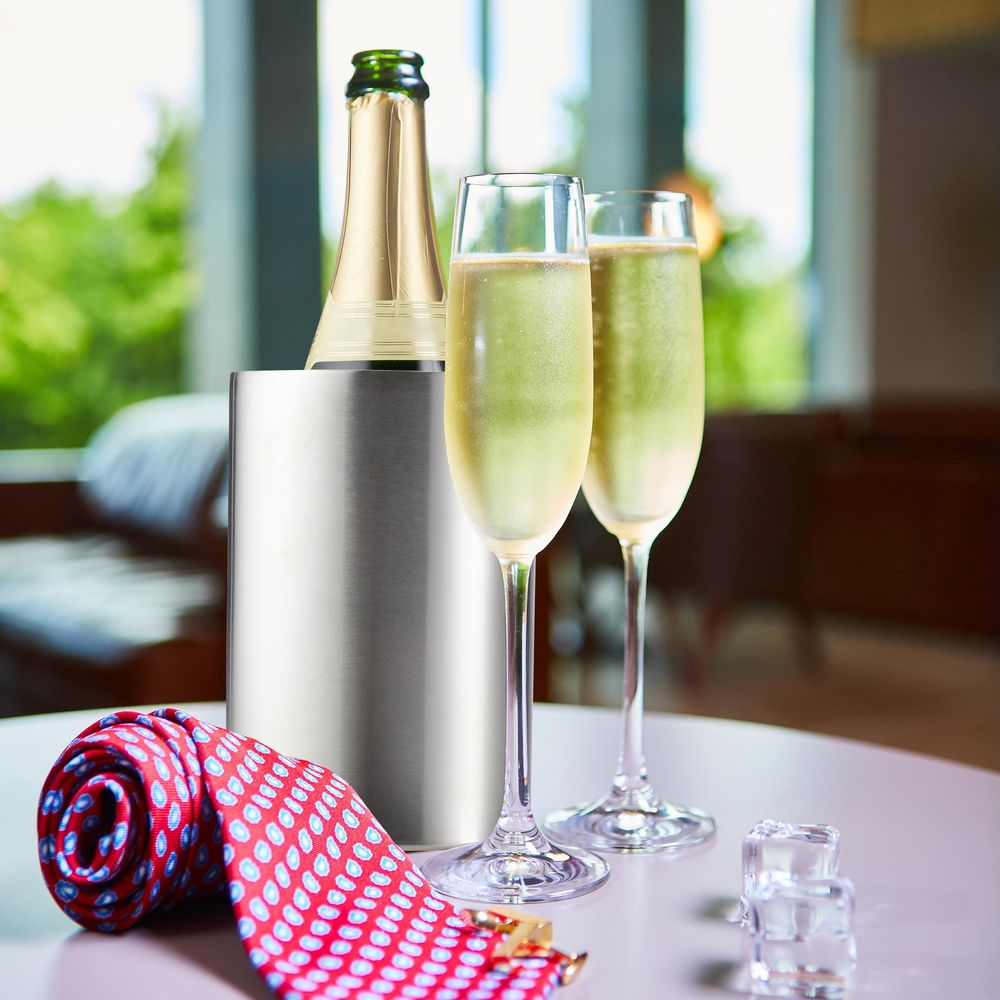 Champagnerkuehler, zwei Glaeser Schaumwein und eine rote Krawatte auf dem Tisch vor hellem Hintergrund.