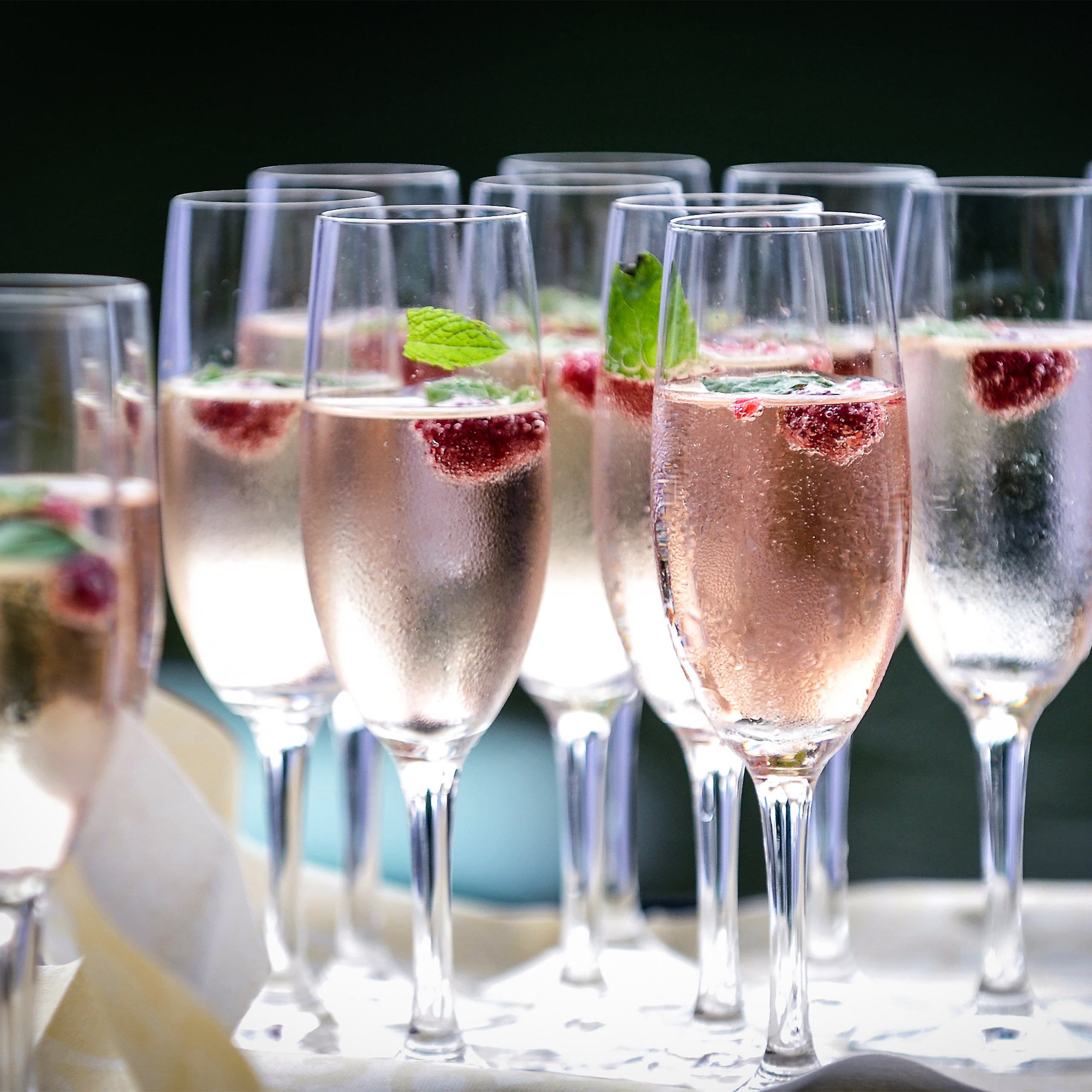 Reihen von Sektgläsern mit sprudelndem Roségetränk, garniert mit Himbeeren und Minzblättern.