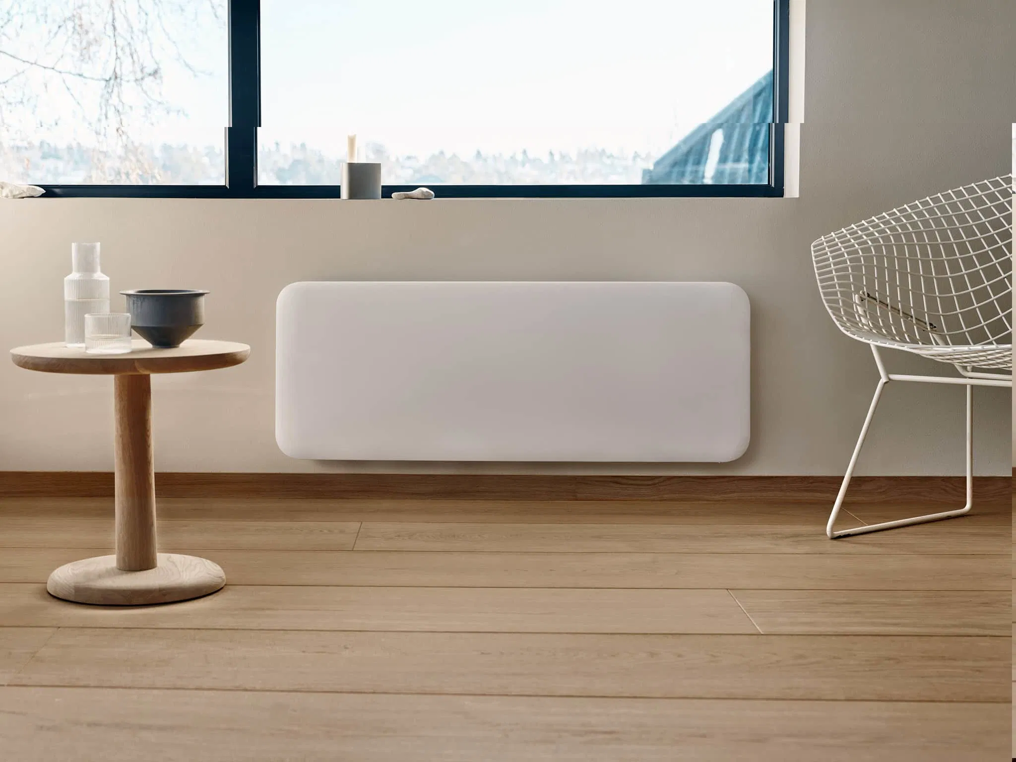 Moderno termosifone bianco su parete grigia, con tavolino in legno a sinistra e sedia in filo metallico bianco a destra.