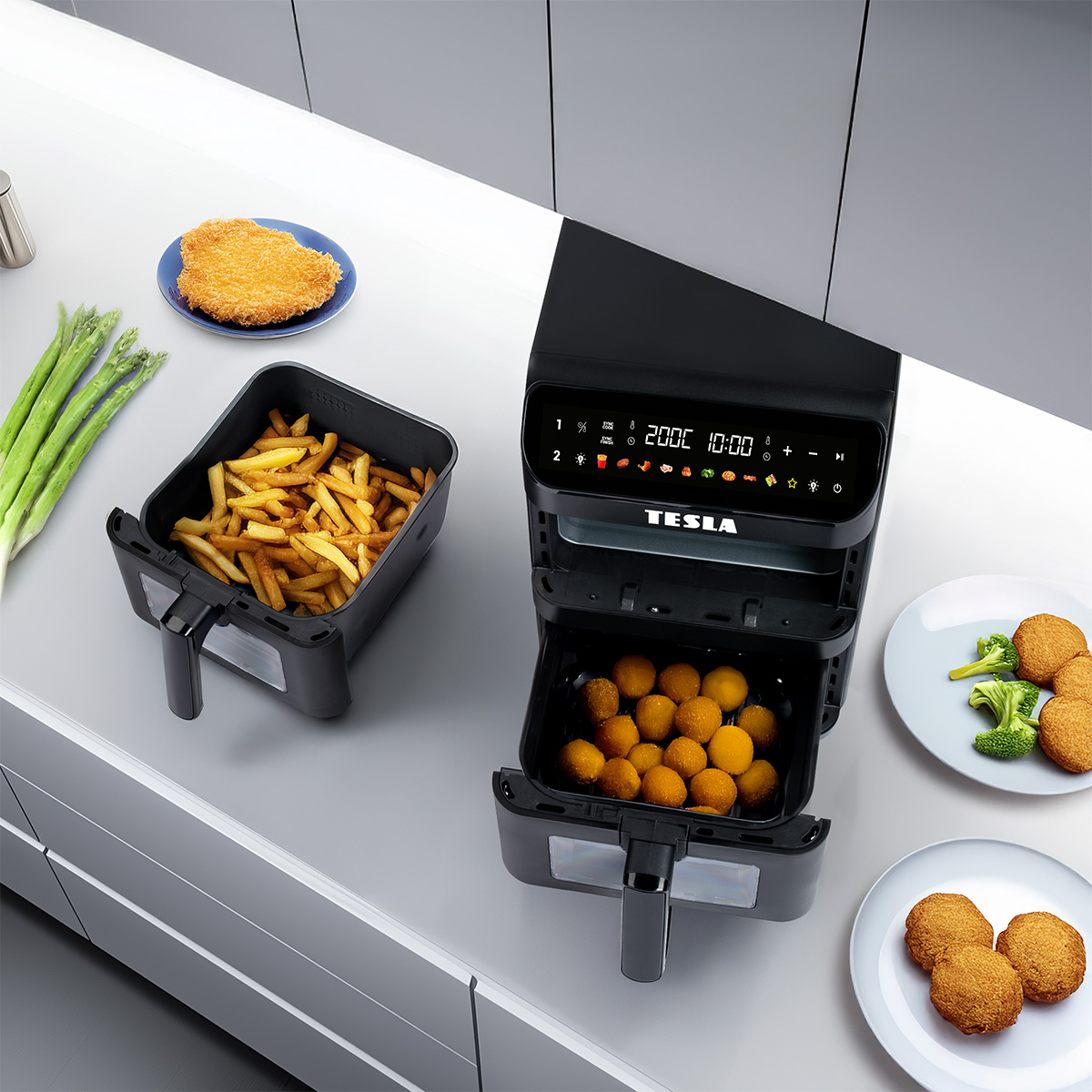Una friggitrice ad aria nera Tesla a doppio cestello su un piano bianco con patatine e nuggets.