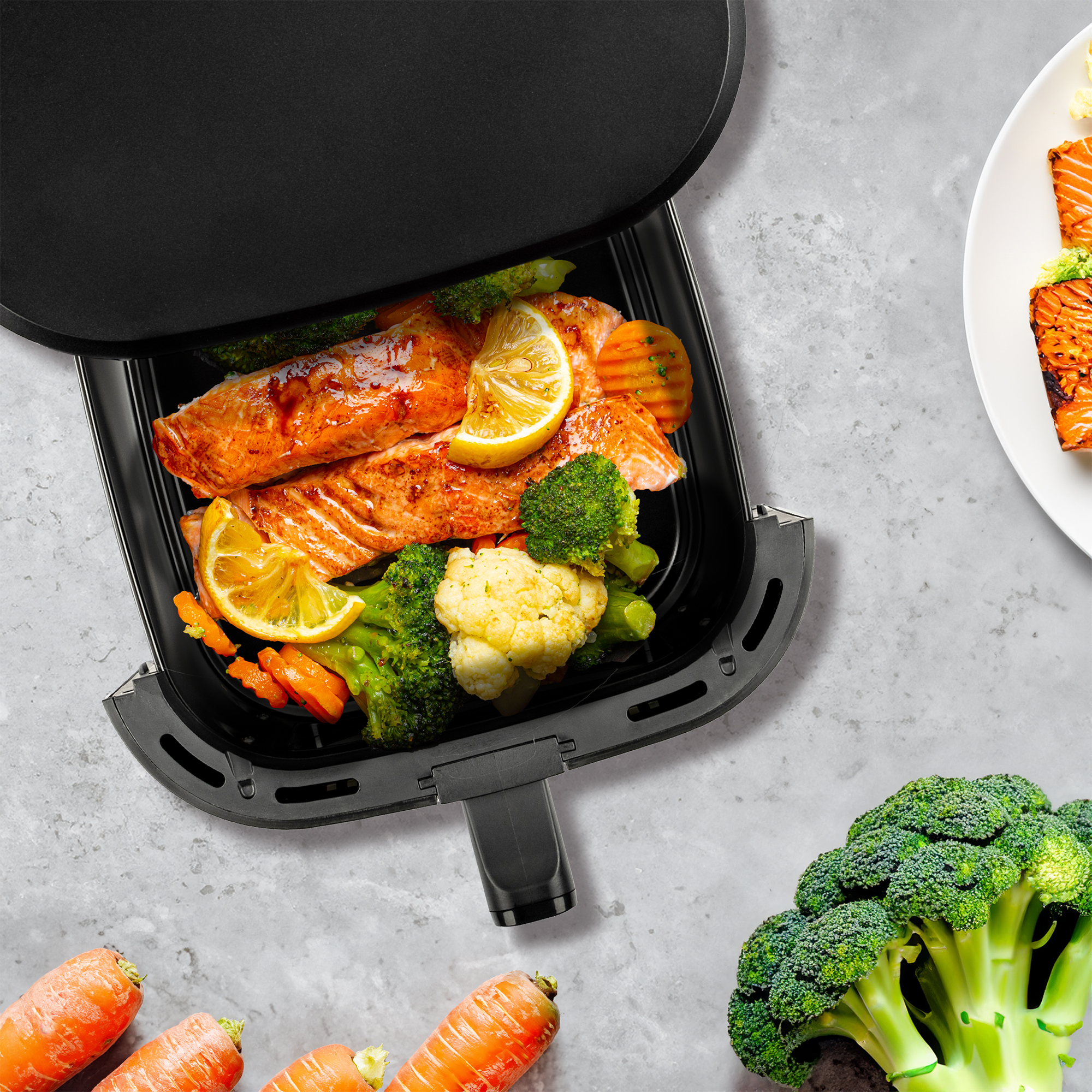 Salmone cotto con broccoli, cavolfiore, carote e fette di limone in una friggitrice ad aria nera.