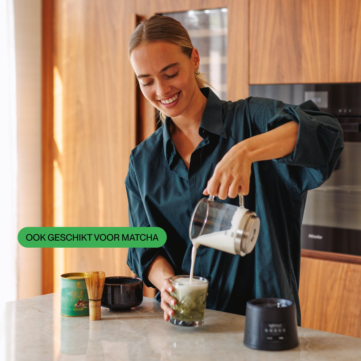 Une femme souriante verse du lait dans une tasse de matcha sur un comptoir.