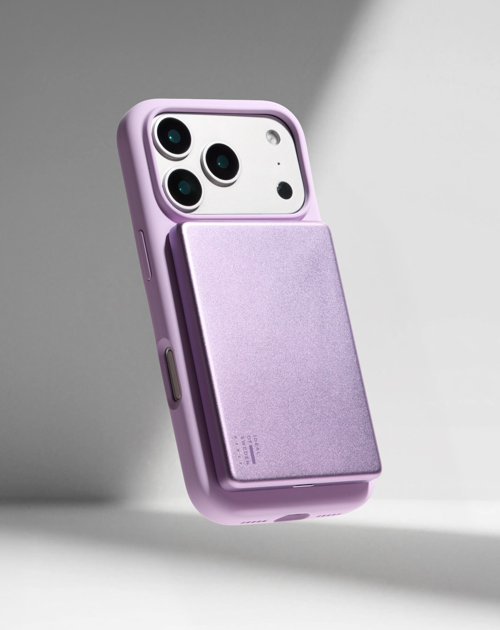 Ein lila Smartphone mit einer passenden lila MagSafe-Powerbank auf der Rückseite vor grauem Hintergrund.
