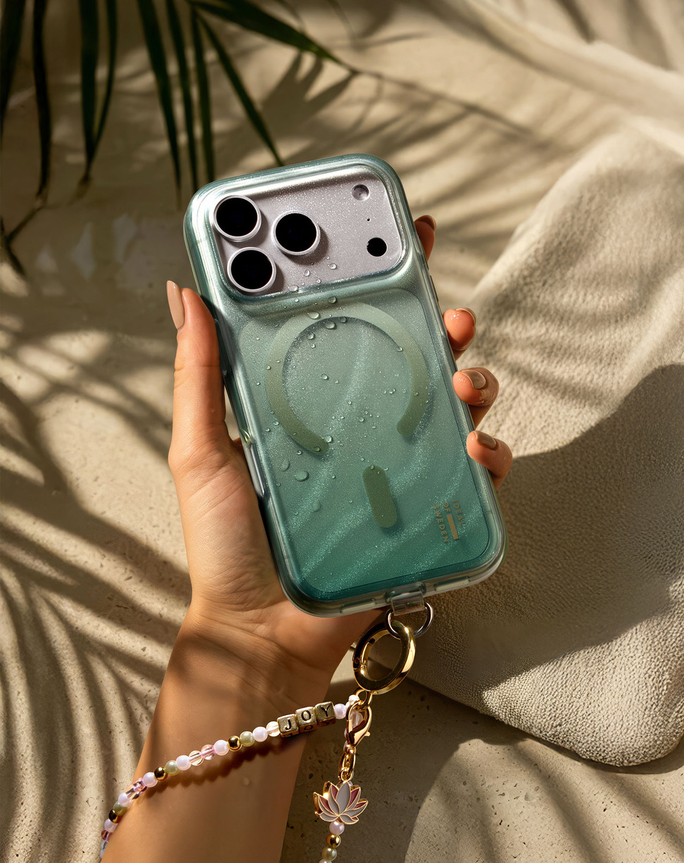 Hand hält glitzernde grüne Smartphone-Hülle mit Armband in sonniger Umgebung.