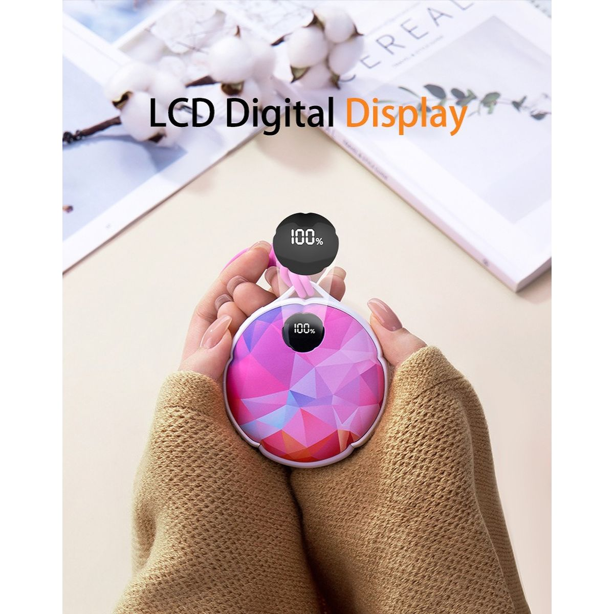 Hände halten ein pinkes, rundes Handwärmegerät mit LCD-Digitalanzeige und 100% Ladung.