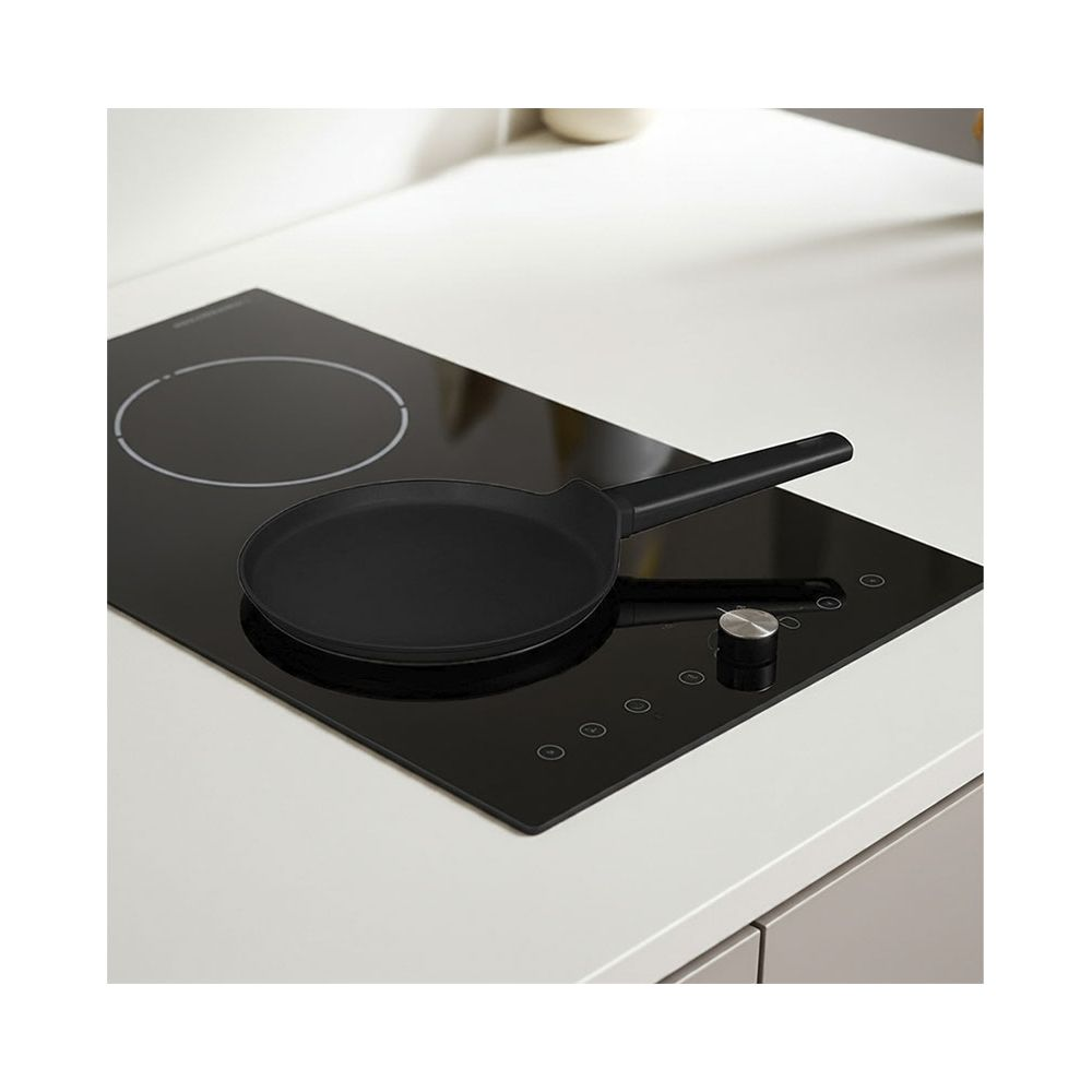 Una padella nera poggia su un piano cottura a induzione moderno e lucido in una cucina luminosa.
