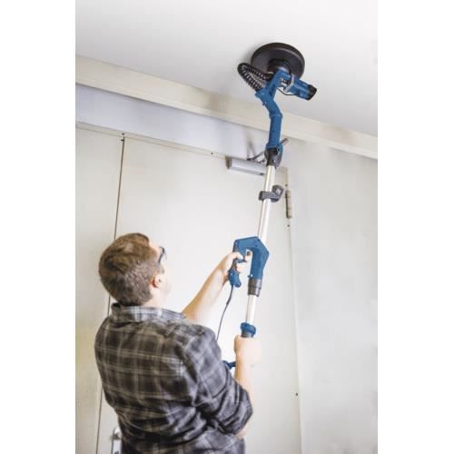Un hombre usa una herramienta eléctrica azul con barra de extensión para lijar un techo.
