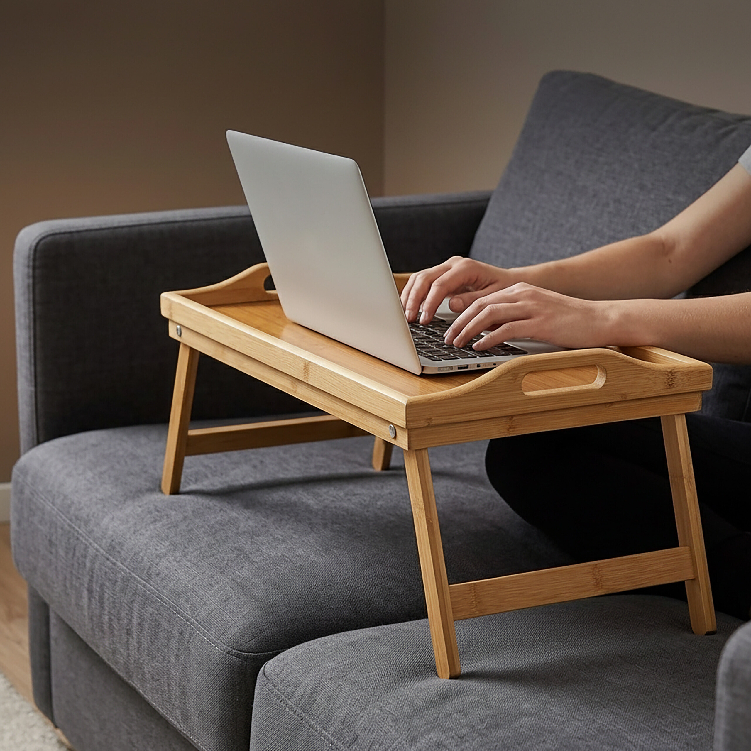 Person arbeitet an einem Laptop auf einem Holztisch, platziert auf einem grauen Sofa.