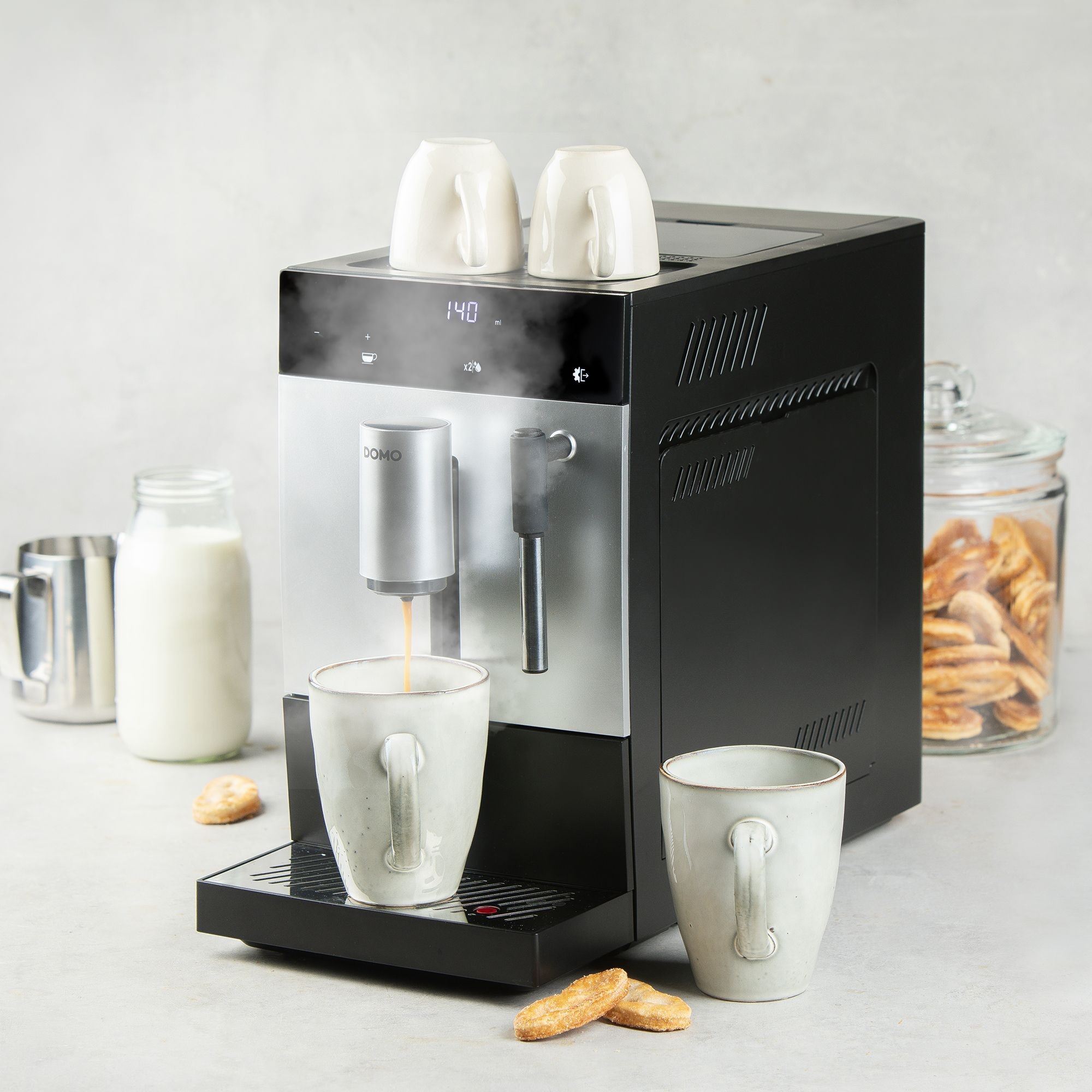 Moderne koffiemachine zet koffie met kopjes, melkfles en koekjes op het aanrecht.