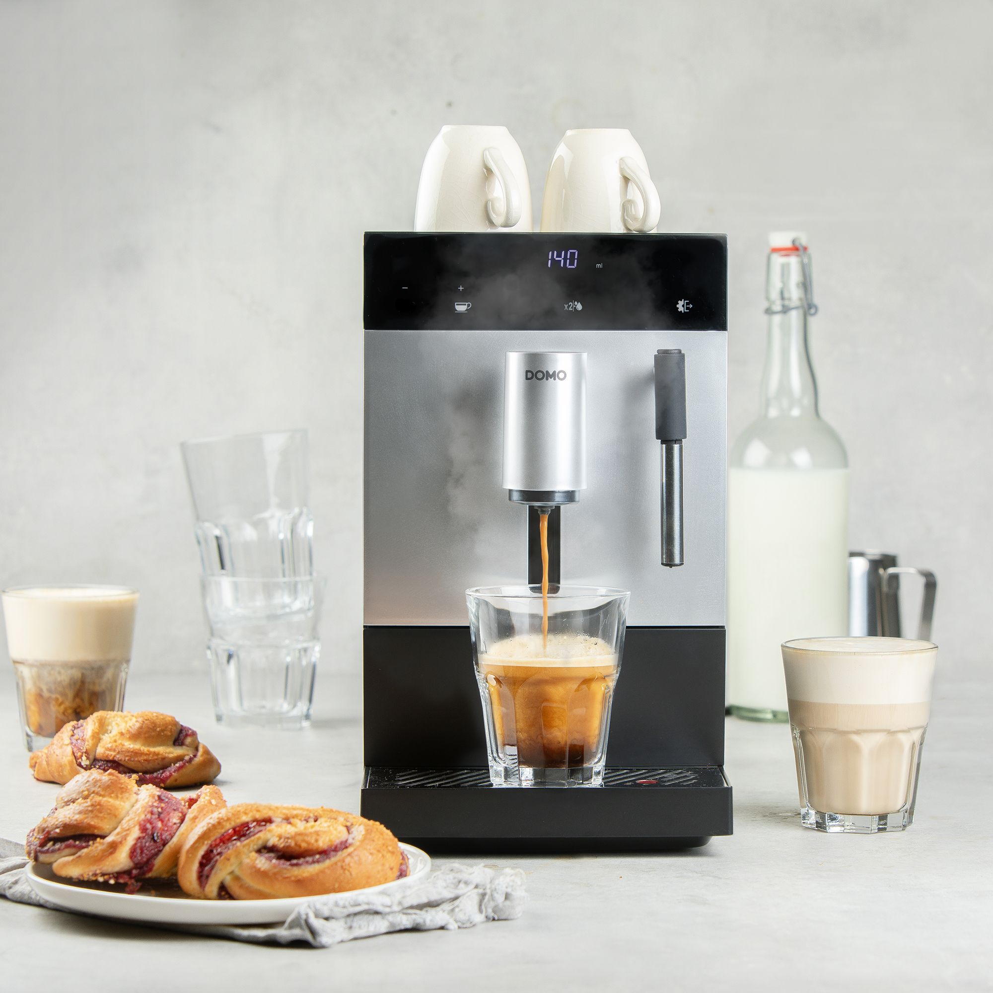 Moderne koffiemachine zet espresso in een glas, met gebak en melk.