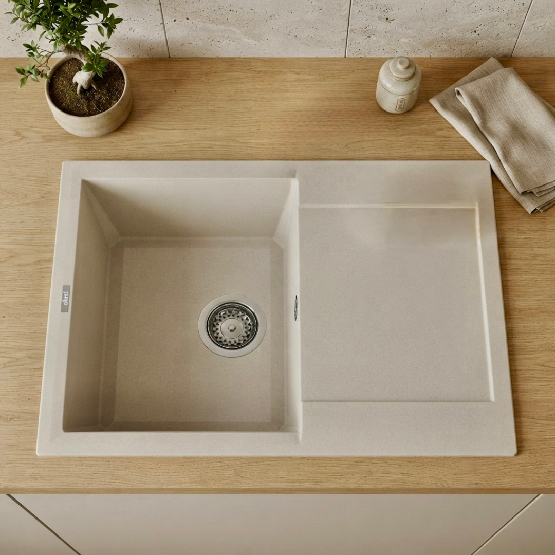 Un lavello da cucina in materiale composito beige con scola piatti su piano in legno, con pianta in vaso e panno.