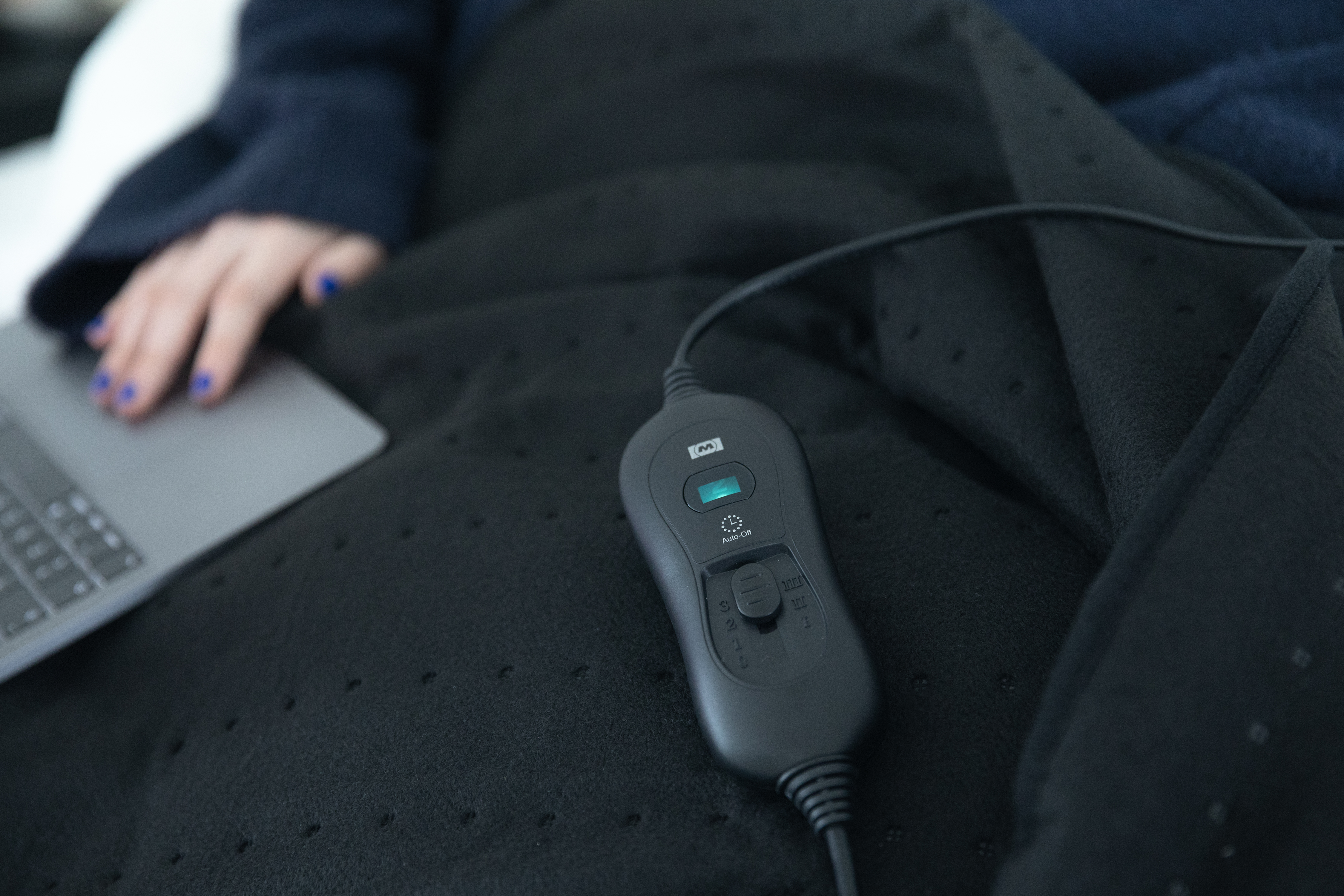 Persona sotto una coperta termica nera con telecomando e laptop.