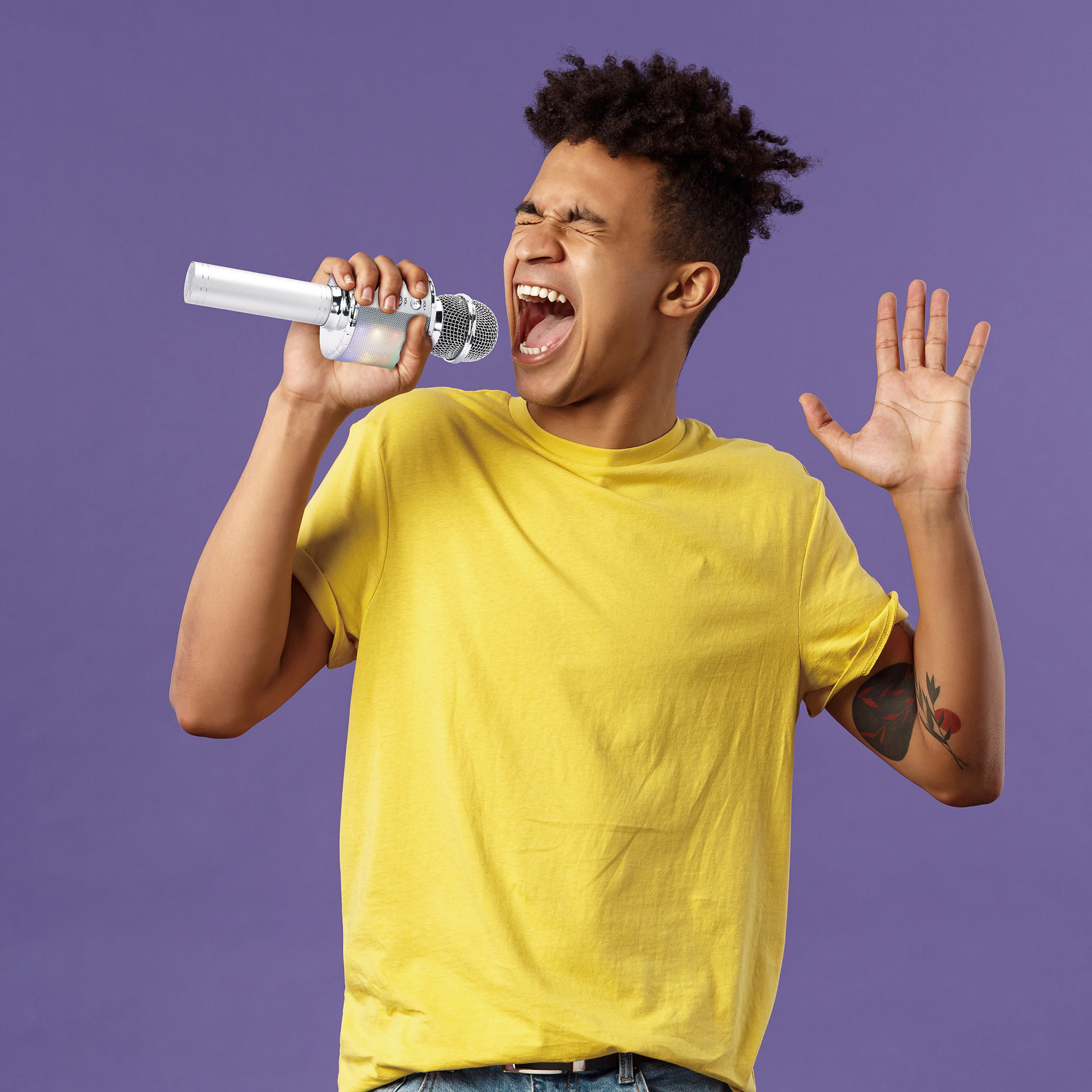 Un jeune homme en t-shirt jaune chante avec passion dans un micro blanc sur fond violet.