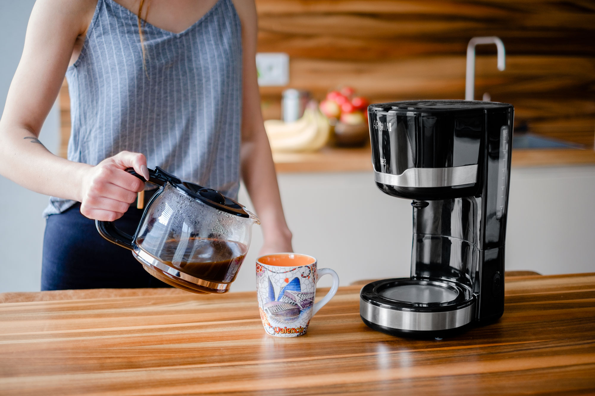 Una donna versa il caffè da una brocca di vetro in una tazza colorata di Valencia accanto a una caffettiera nera.