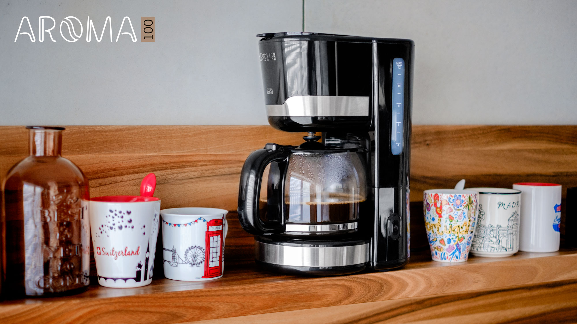 Caffettiera a filtro nera con caraffa in vetro e tazze colorate su ripiano in legno.