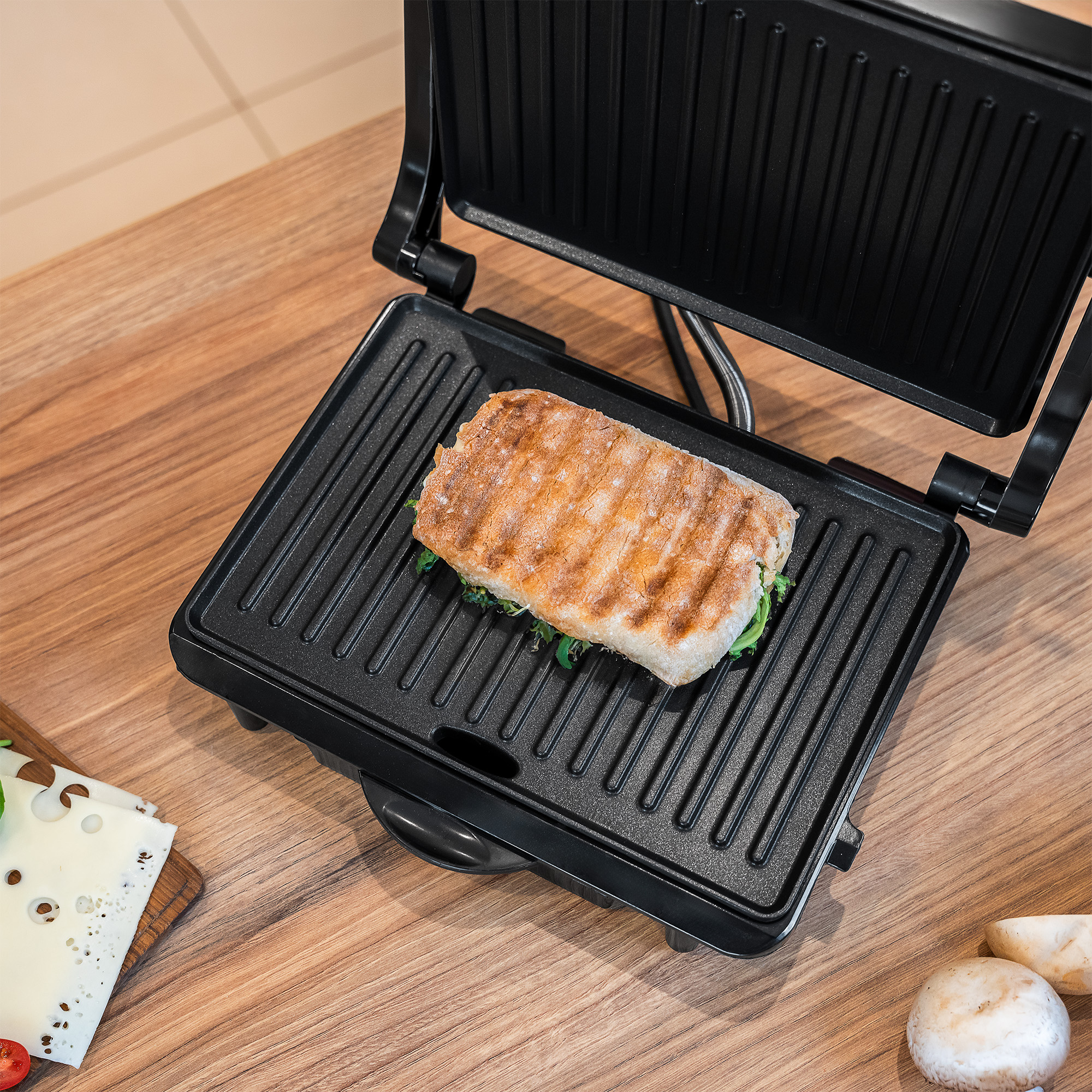 Opieczona kanapka panini spoczywa w otwartym czarnym grillu elektrycznym na drewnianym stole.