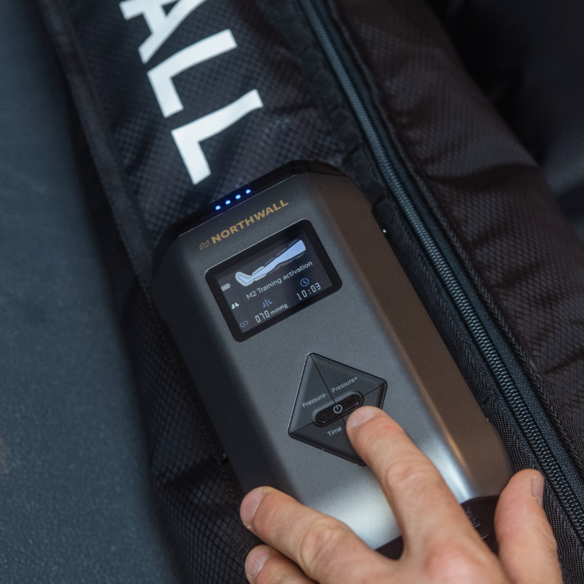 Une main appuie sur le bouton d'un appareil noir Northwall avec écran, posé sur un sac noir.