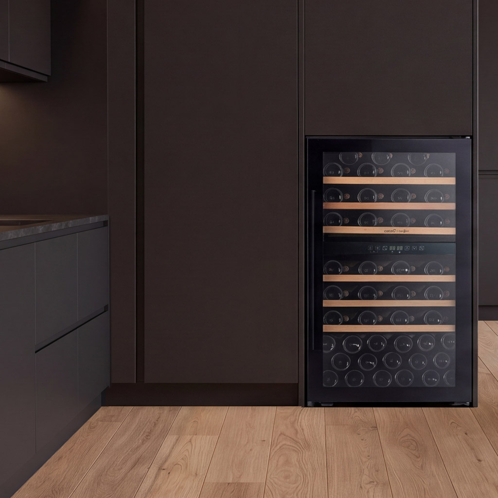 Un enfriador de vinos empotrable con estantes de madera está en una cocina moderna con armarios oscuros y suelo de madera.