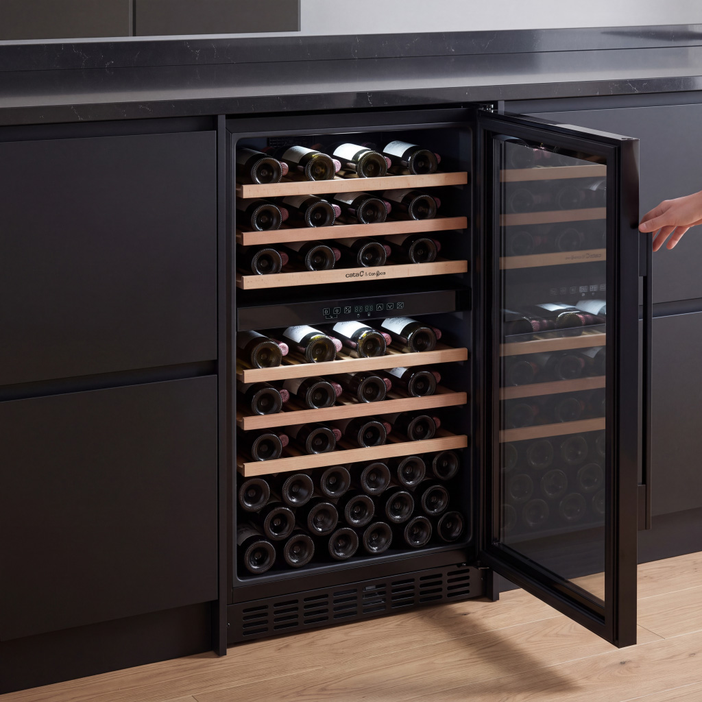 Un enfriador de vino abierto con estantes de madera y numerosas botellas en una cocina negra moderna.
