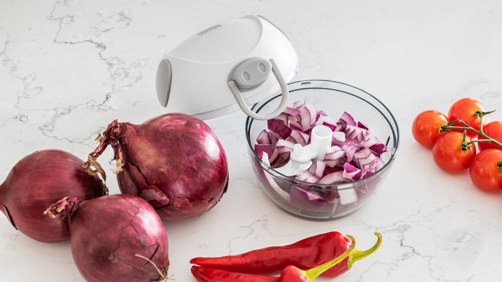 Biała siekaczka do warzyw z posiekaną czerwoną cebulą, całymi cebulami, papryczkami chili i pomidorami.