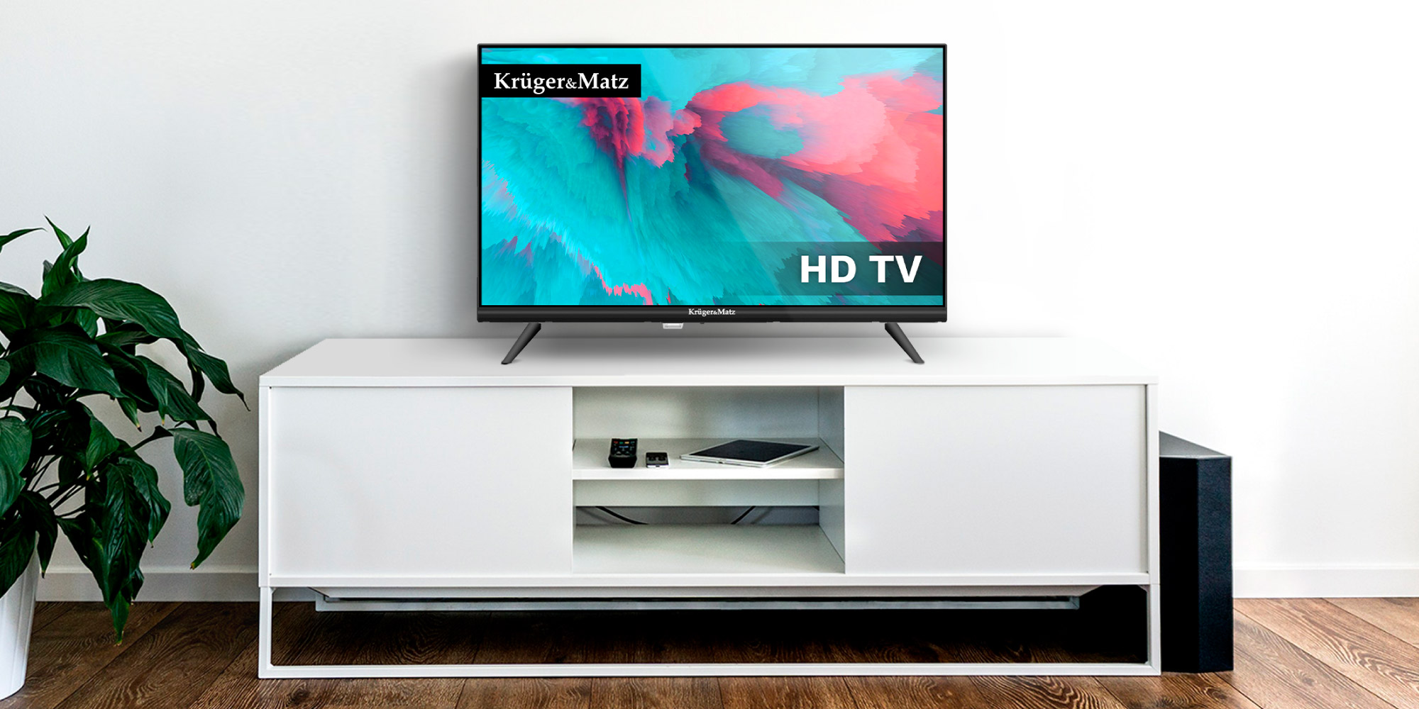 Telewizor HD z kolorowym ekranem stoi na białej szafce RTV w jasnym pokoju.