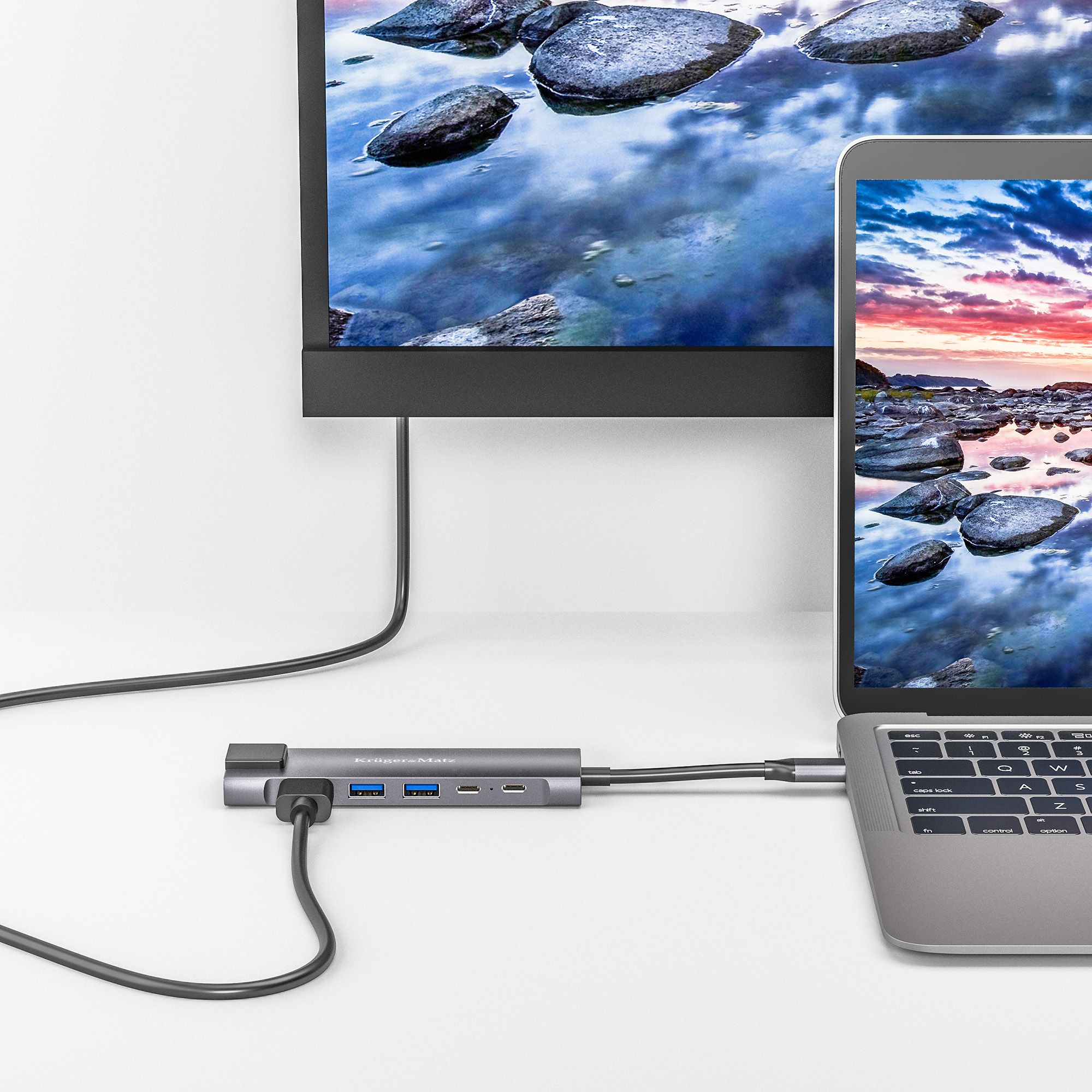 Laptop i monitor zewnętrzny podłączone do szarego huba USB-C na białym biurku.
