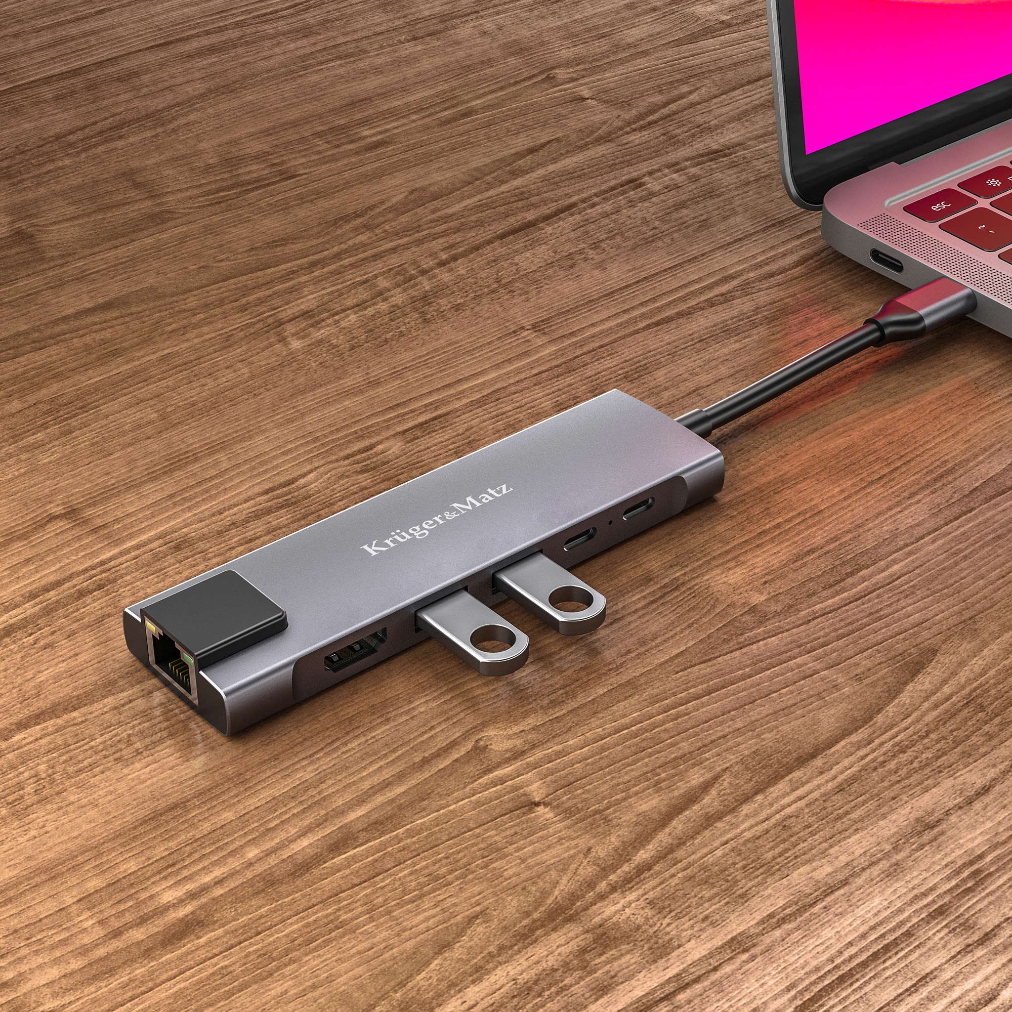 Szary hub USB-C Kruger&Matz na drewnianej powierzchni, podłączony do laptopa.