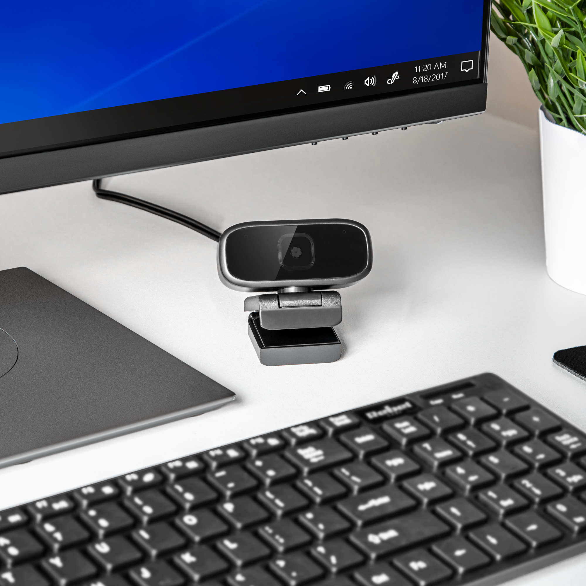 Kamera internetowa stoi na biurku przed monitorem komputera, obok klawiatury.